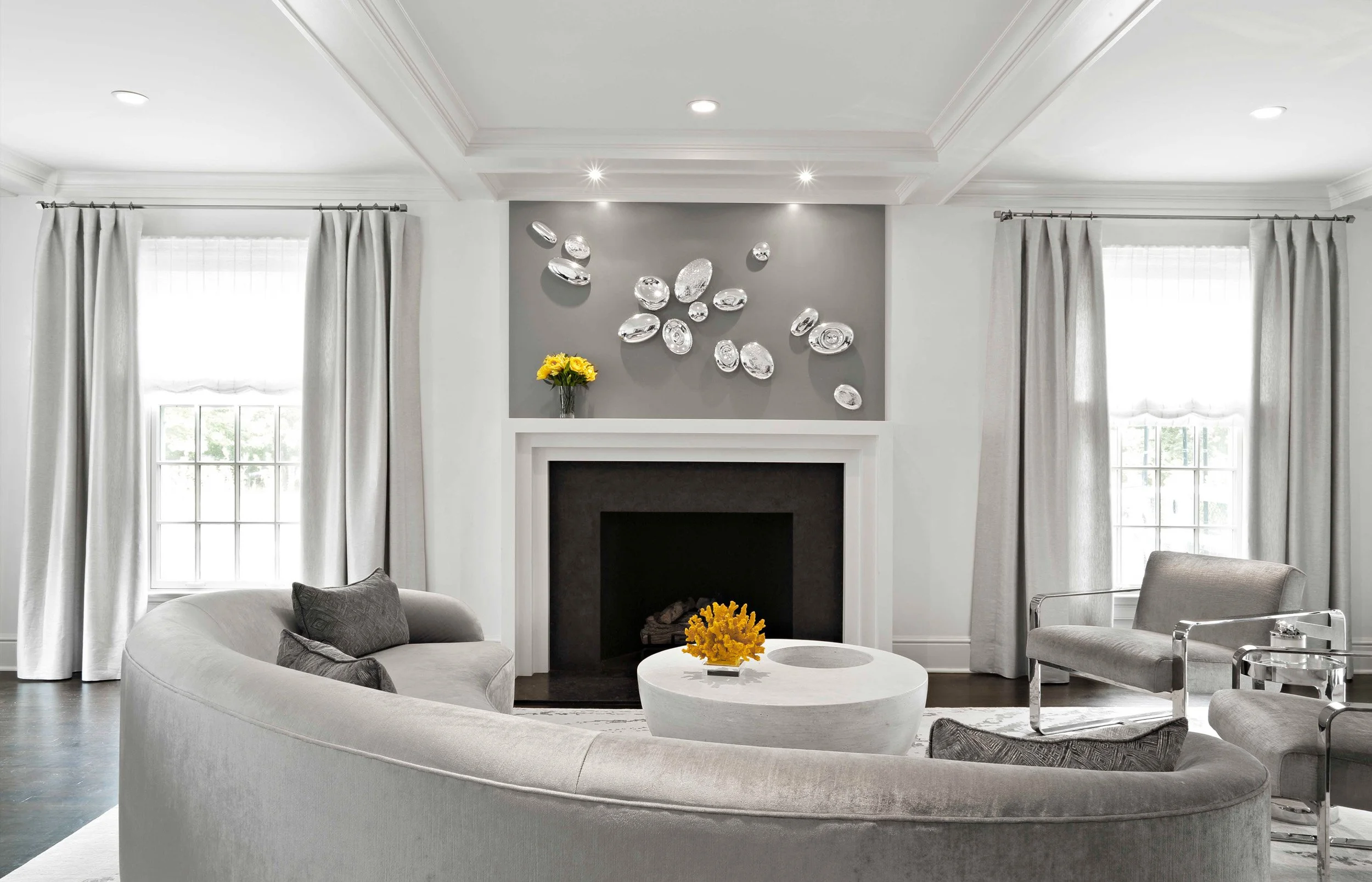 Luminosus Designs created a iving room at the Meeting House in Greenwich, CT featuring a curved sofa, fireplace surround, and layered neutral palette.