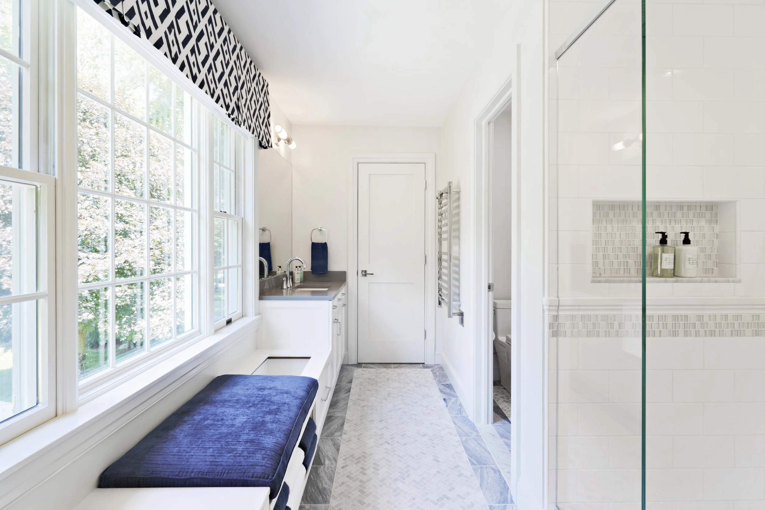 Wide view of a bright Jack and Jack bathroom at the Dann Farm home in Pound Ridge, NY designed by Luminosus Designs, featuring white cabinetry, marble tile flooring, and built-in bench seating.