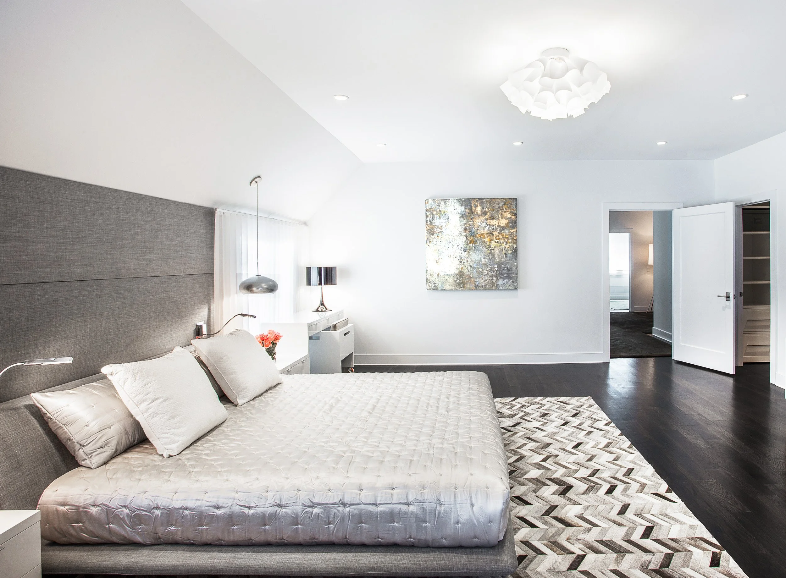 Wide bedside view of the primary bedroom showing the platform bed, textured wall panels, and modern artwork.
