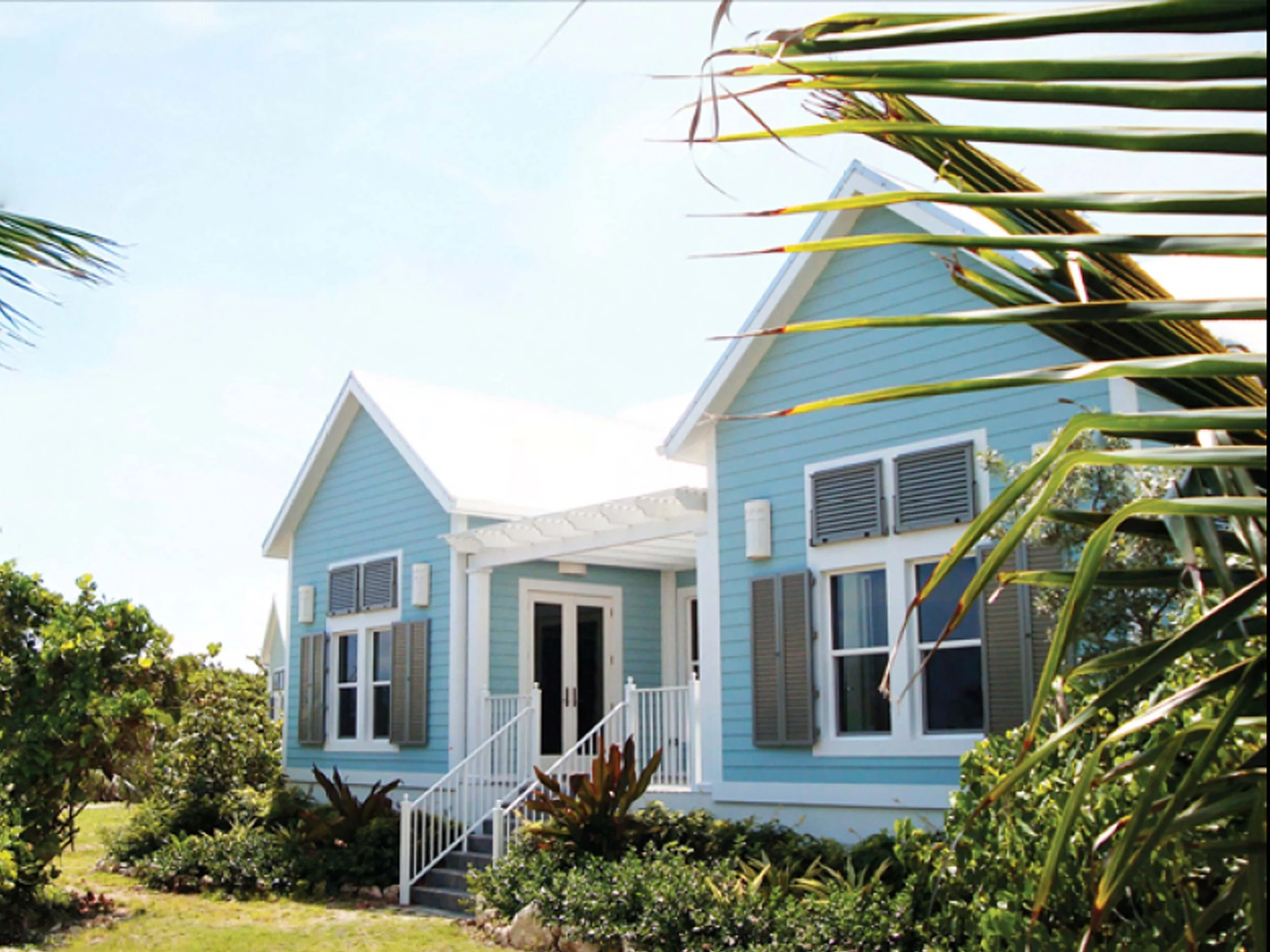 Coastal guest villas in Grand Cayman with light blue siding and tropical landscape.
