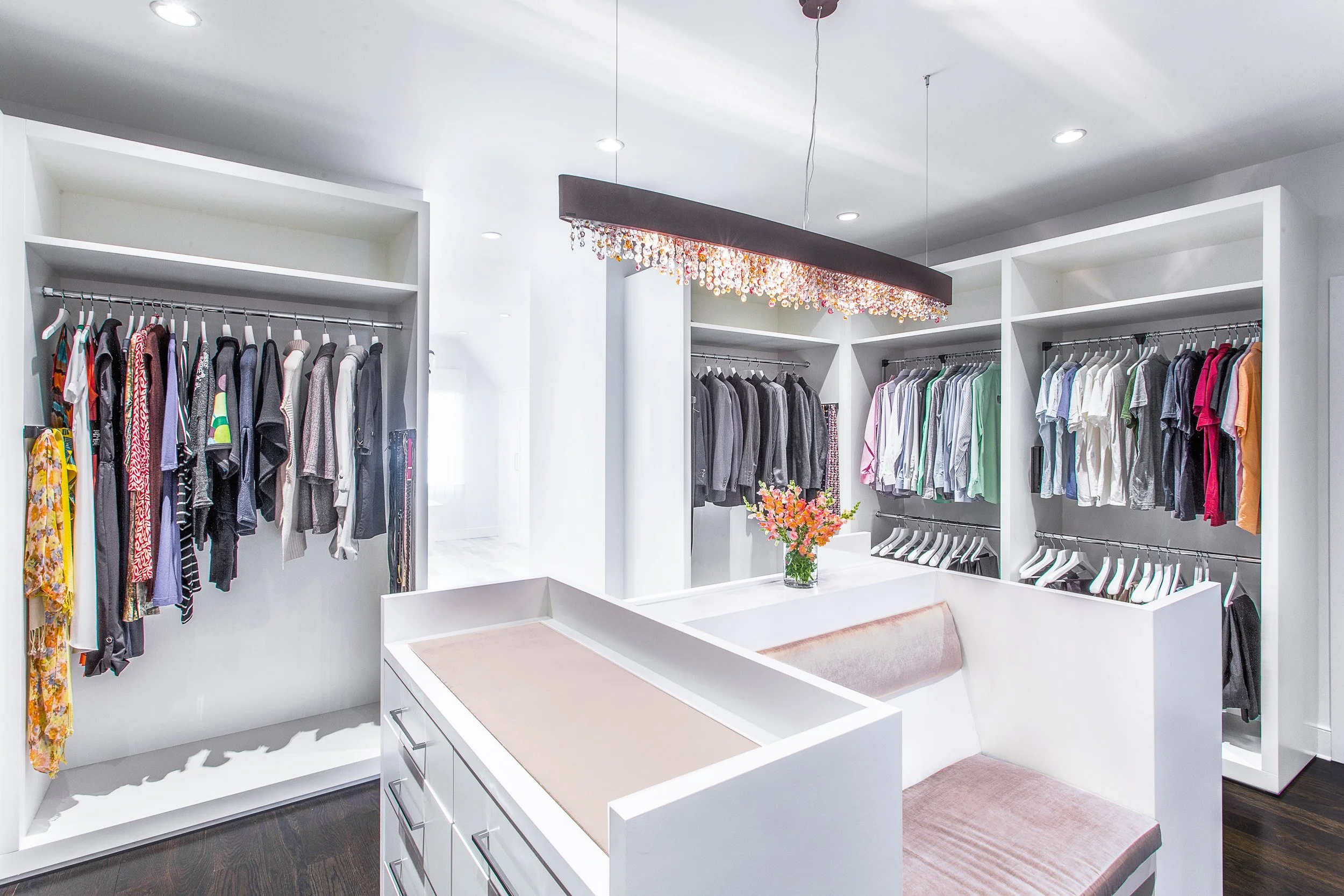 Wide view of the custom closet storage with hanging rods, open shelving, and a center island for folded items.