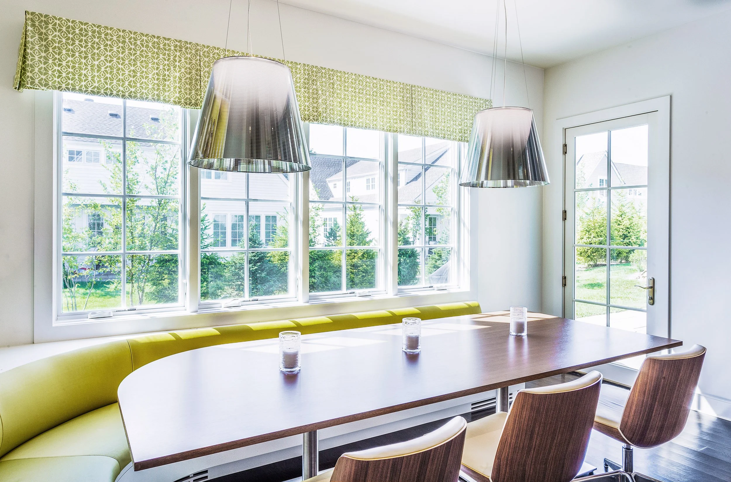 Close-up view of the breakfast banquette by the windows with chrome pendants and a warm wood tabletop.