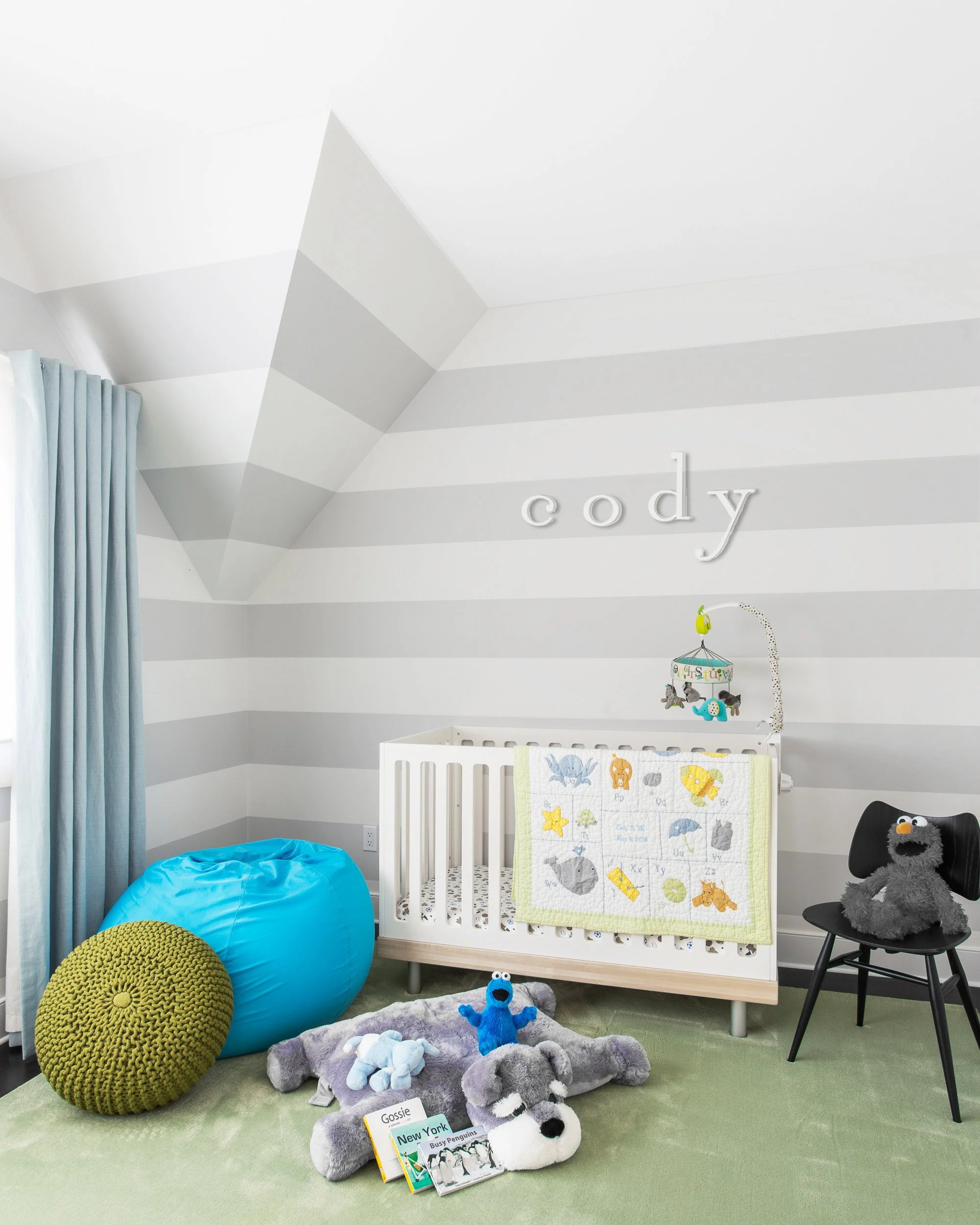 Close-up of a nursery corner with striped walls, a crib, and relaxed seating for a soft, playful look in boy's bedroom in Kensett House in Darien, CT. 