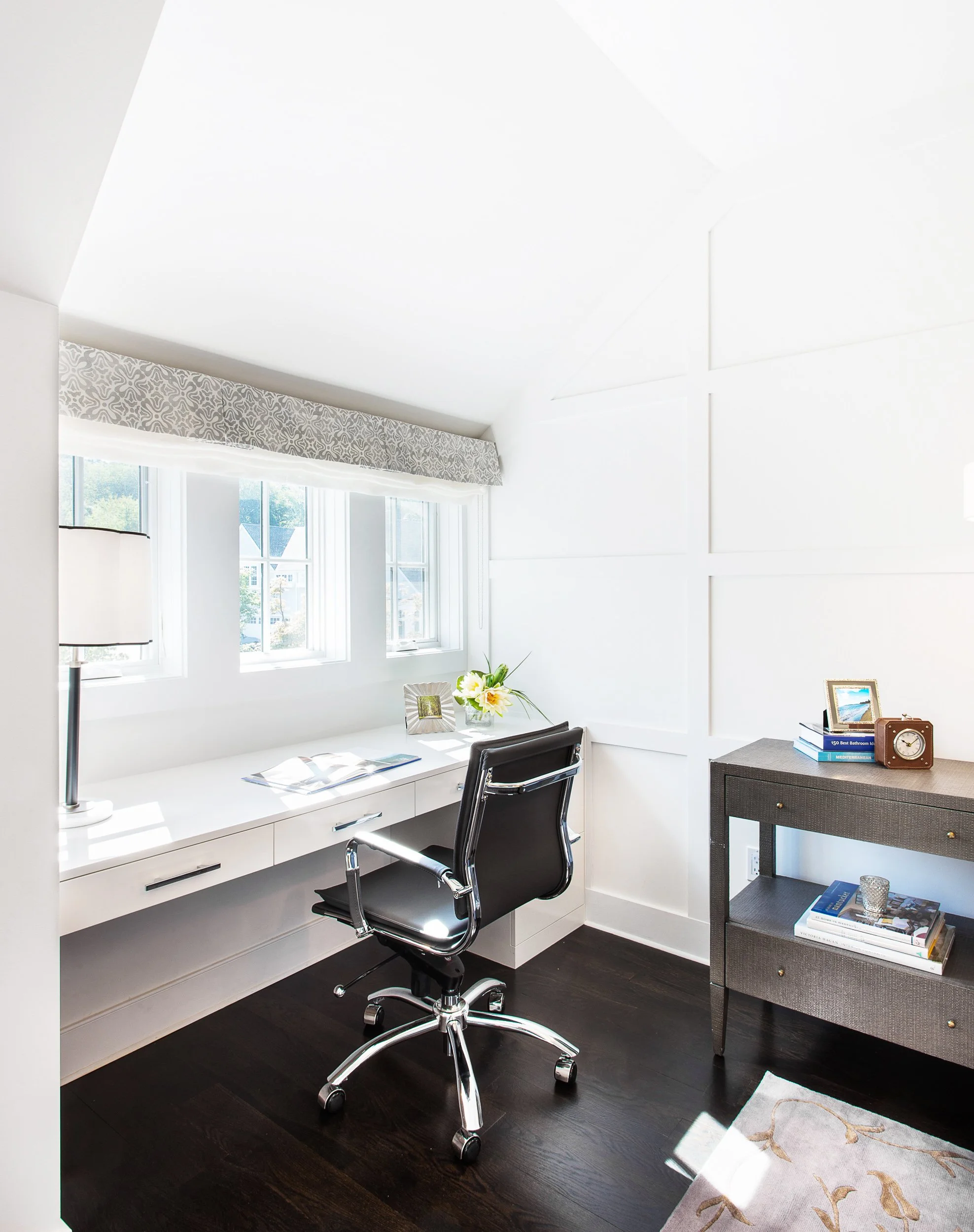 Close-up view of a writing desk set under large windows with a task chair and minimal styling.
