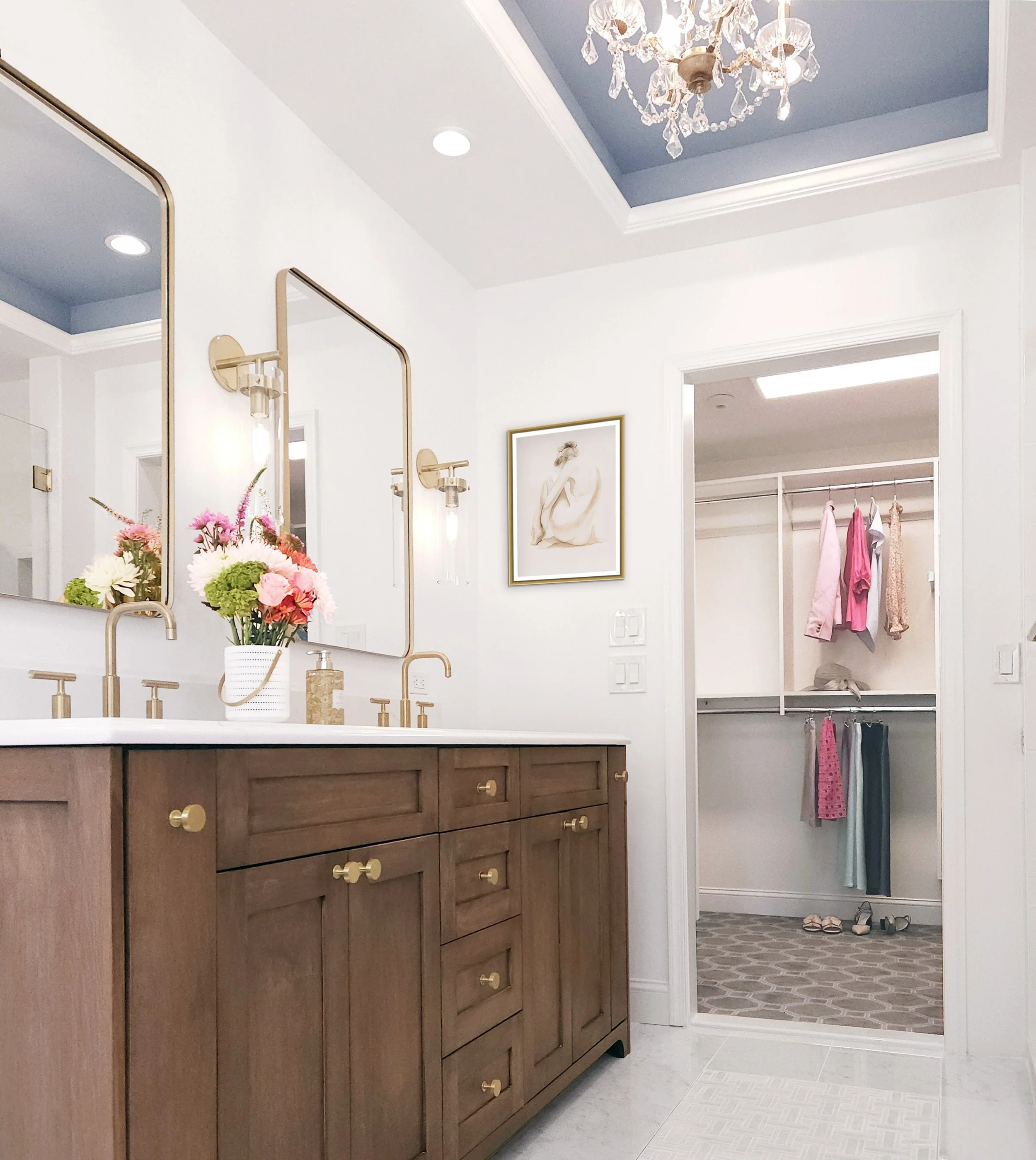 Primary bathroom vanity with wood cabinetry, brass hardware, and blue cove ceiling with chandelier in Carlyle Court in Princeton, NJ.