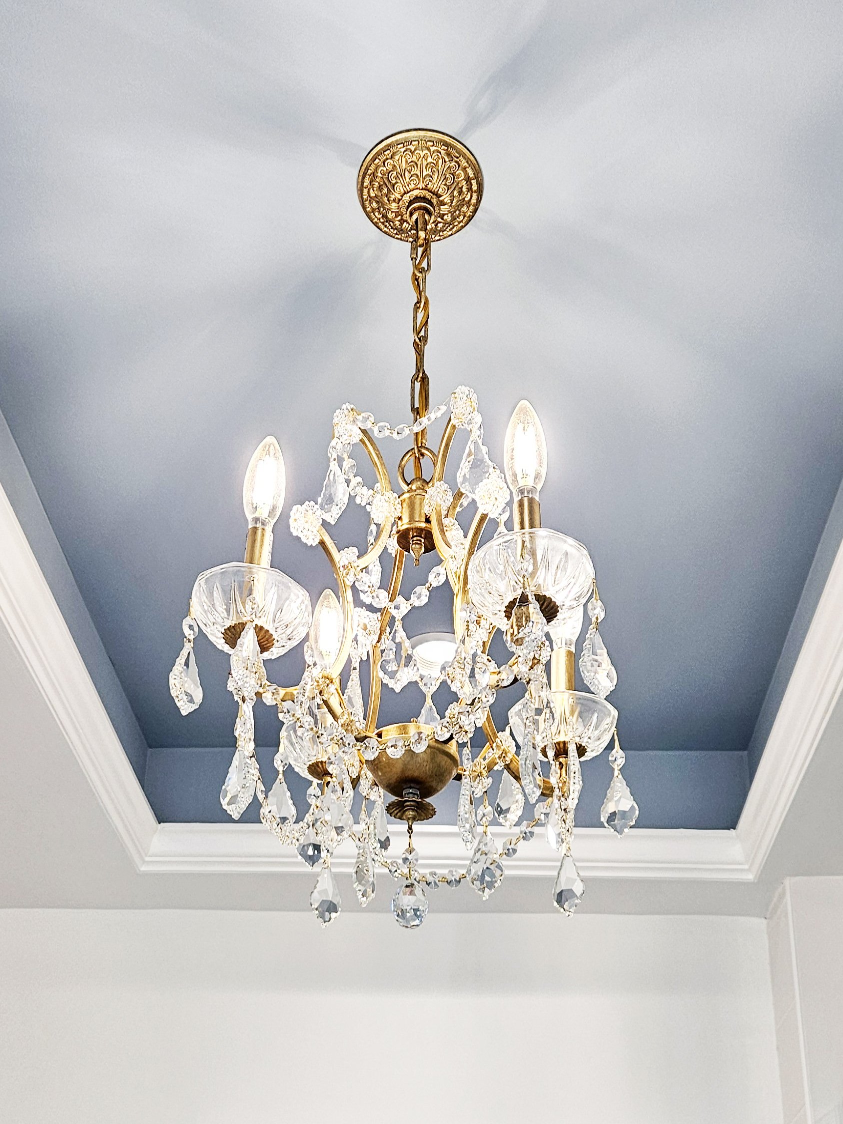 Crystal chandelier in a blue cove ceiling adding elegance to the Carlye Court residence in Princeton, NJ primary bathroom.