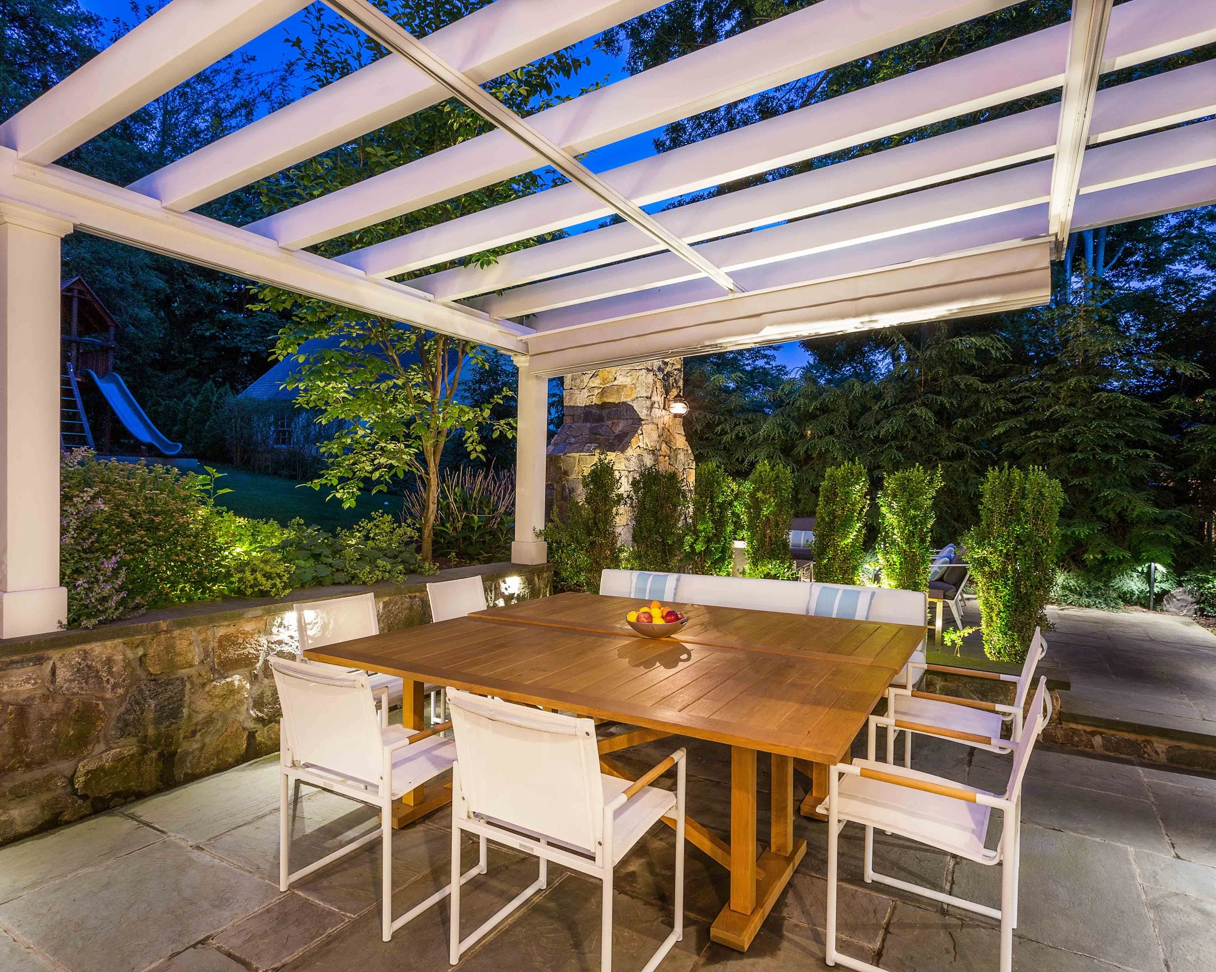 Evening view of outdoor dining area with pergola shade retracted at the Indian Field Outdoor project in Greenwich, CT.