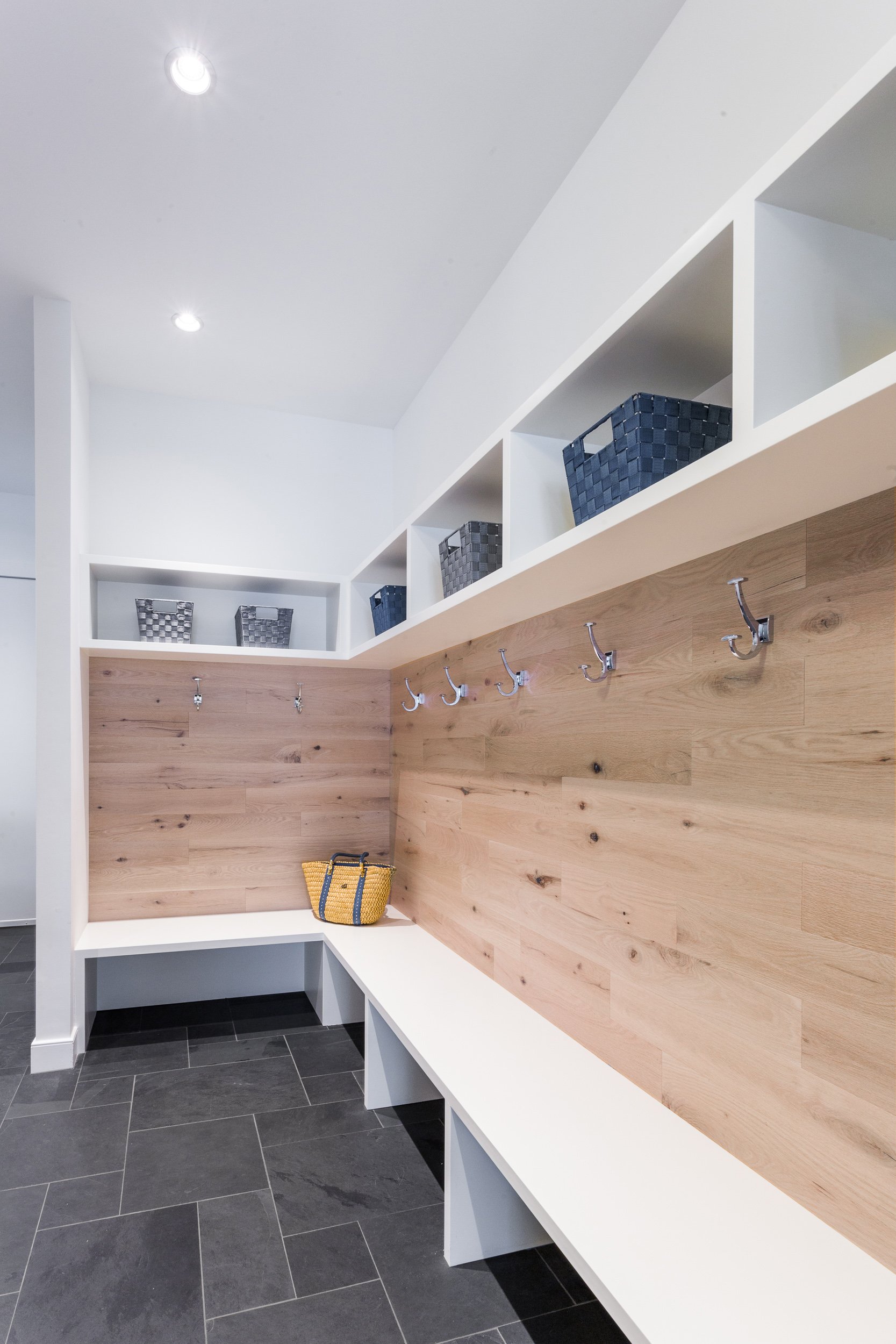 Wide view of a mudroom with built-in bench seating, oak plank wall with hooks, and open cubby storage above. Designed by Luminosus Designs.