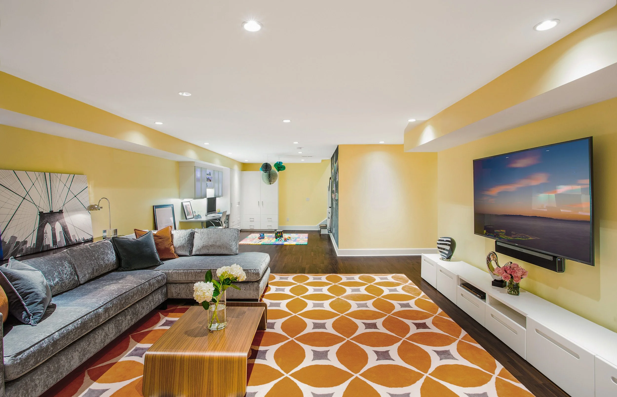 Wide view of a finished basement recreation room with comfortable seating, a media wall, and open space for gathering in Kensett House in Darien, CT.  Designed by Luminosus Designs.