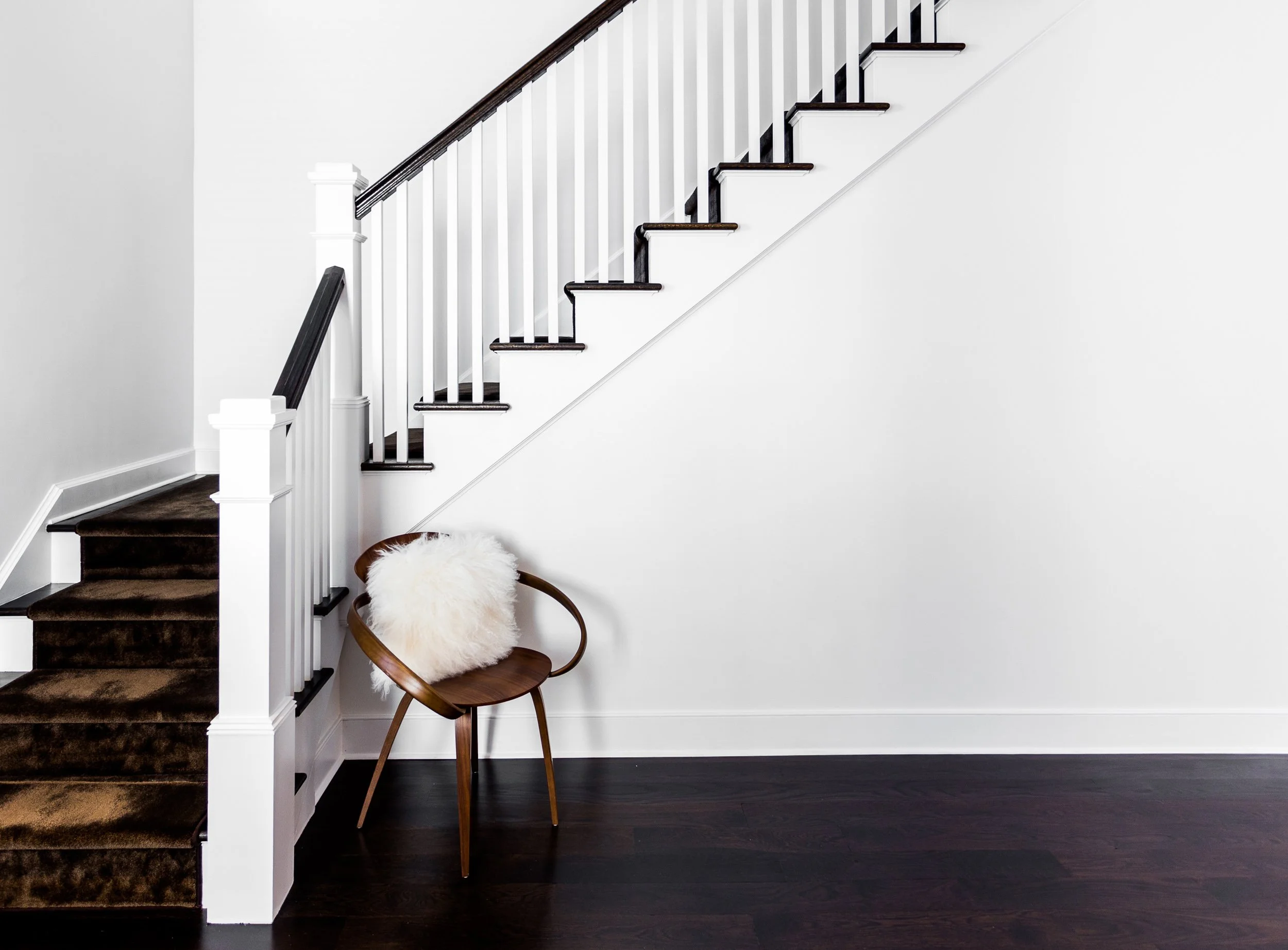 Close-up view of the foyer staircase with dark wood treads, white balusters, and a soft seating vignette.