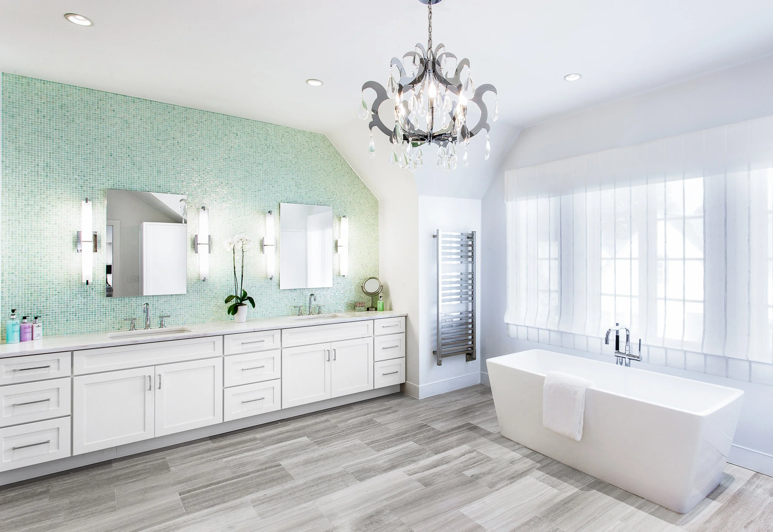 Wide view of a primary bathroom with a long double vanity, green mosaic tile feature wall, and modern vertical sconces in Kensett House in Darien, CT.  Designed by Luminosus Designs.