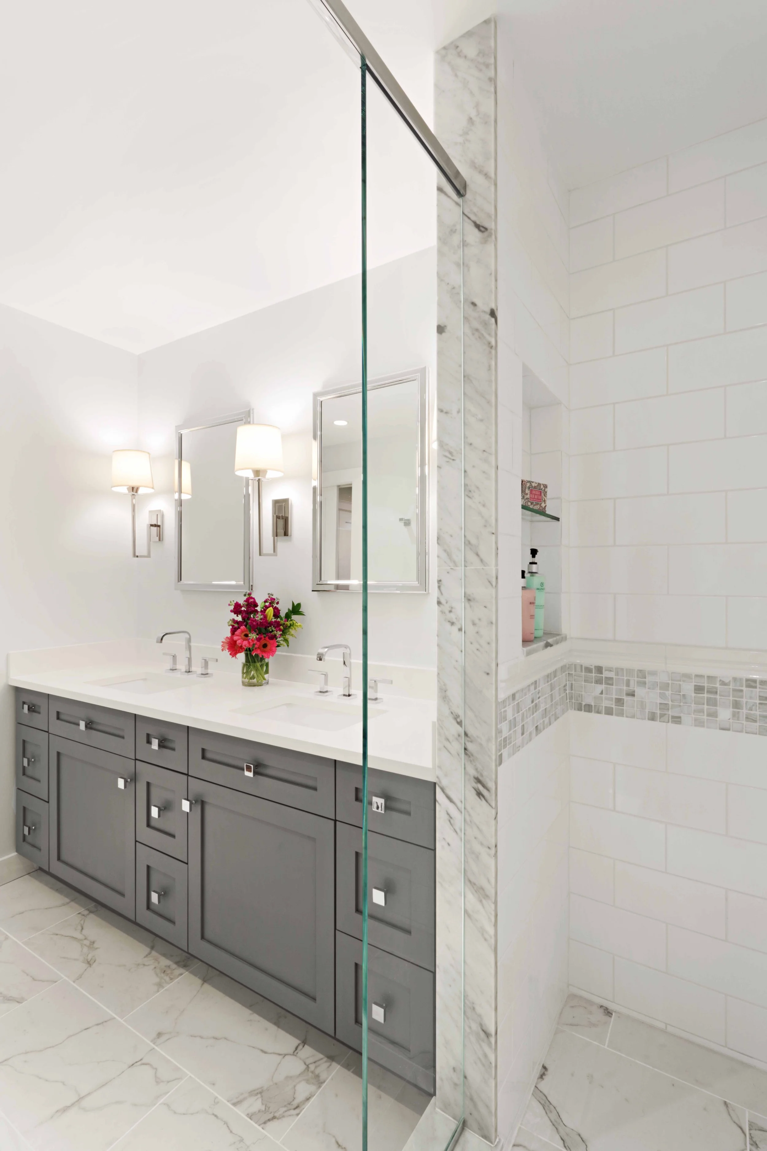 Close-up of a glass-enclosed shower with white subway tile, marble accents, and chrome fixtures in a primary bathroom.