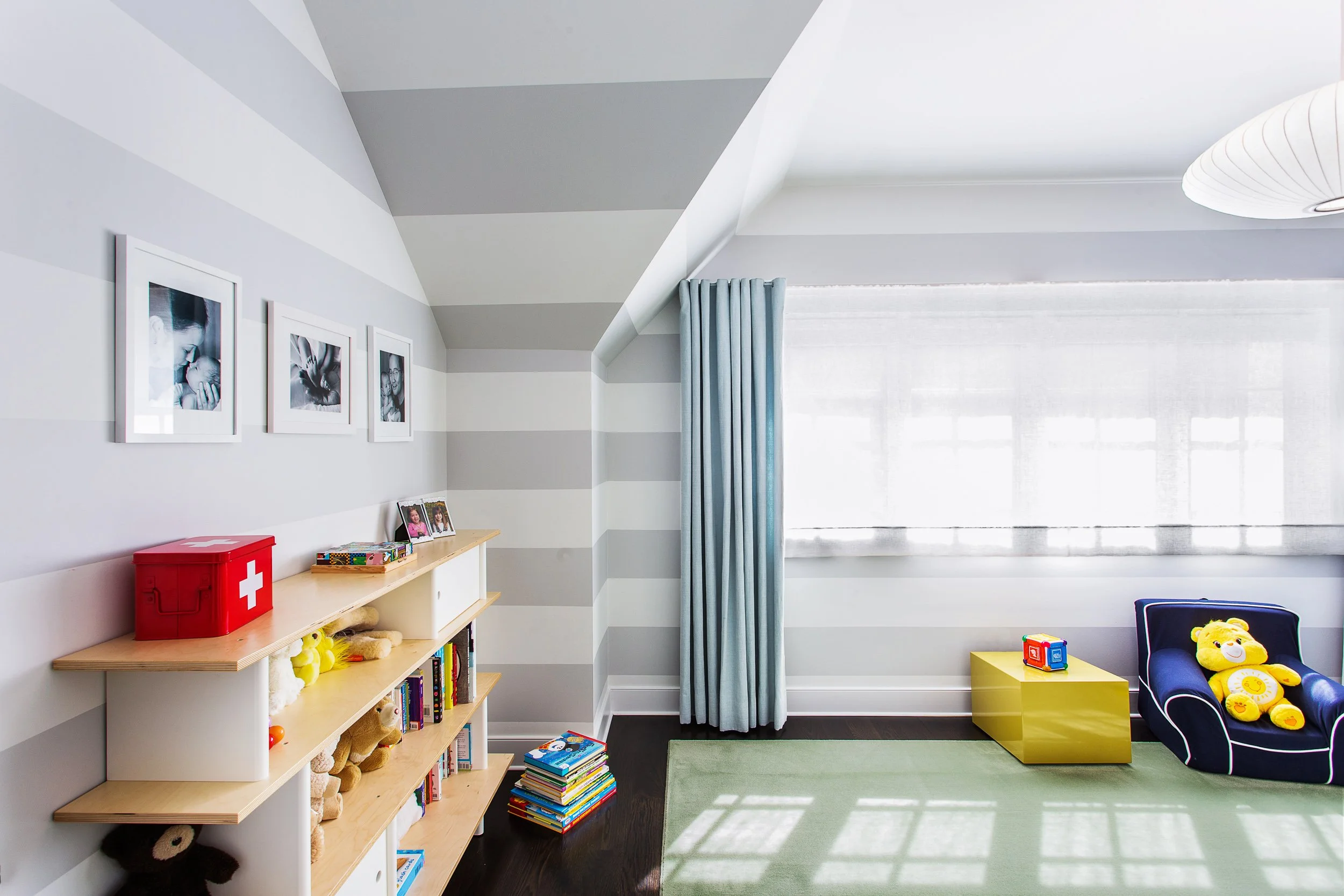 Wide view of a boys bedroom play area with striped wall treatment, low shelving, and kid-friendly seating. Designed by Luminosus Designs.
