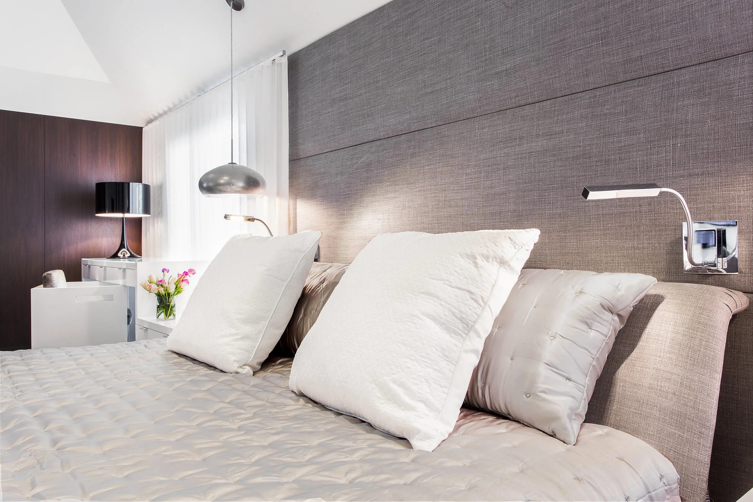Close-up of layered pillows and an upholstered headboard with a sleek wall-mounted reading light in Kensett residence, Darien CT.
