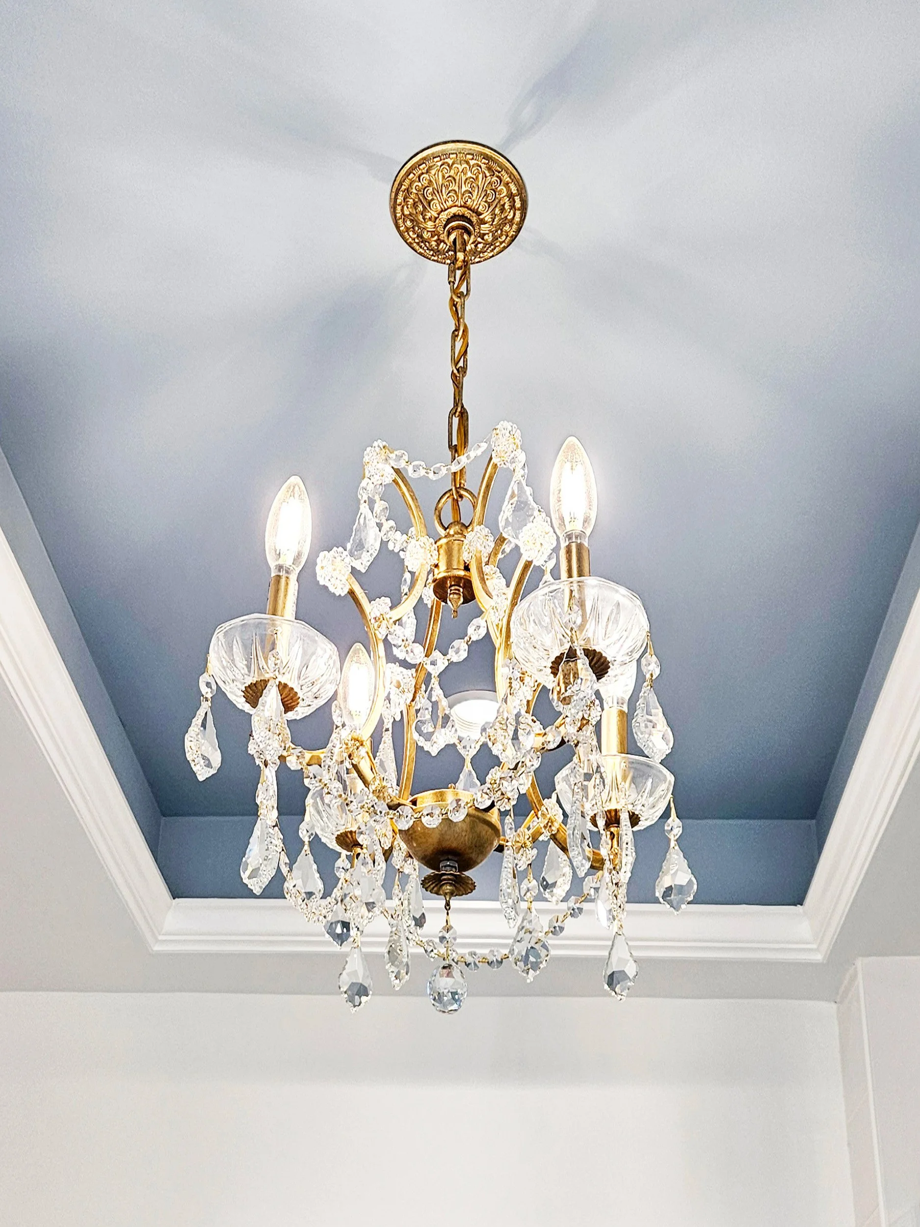 Crystal chandelier in a blue cove ceiling adding elegance to the Carlye Court residence in Princeton, NJ primary bathroom.