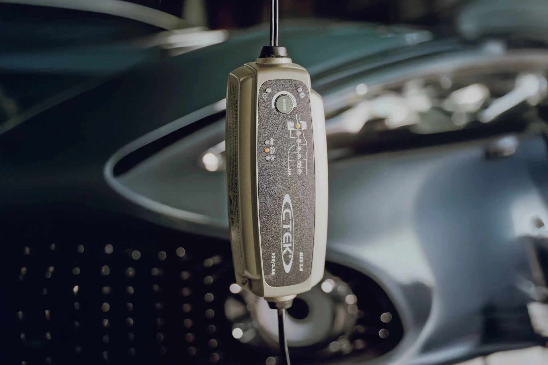 A car diagnostic scanner hanging in front of a car's open hood.