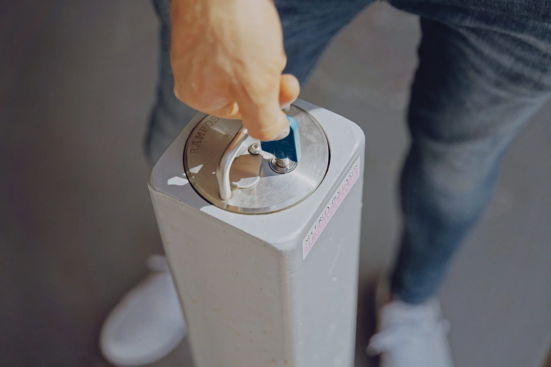 A person is pulling a handle on a large, white container, likely for dispensing a liquid or beverage, with part of their jeans and shoes visible.