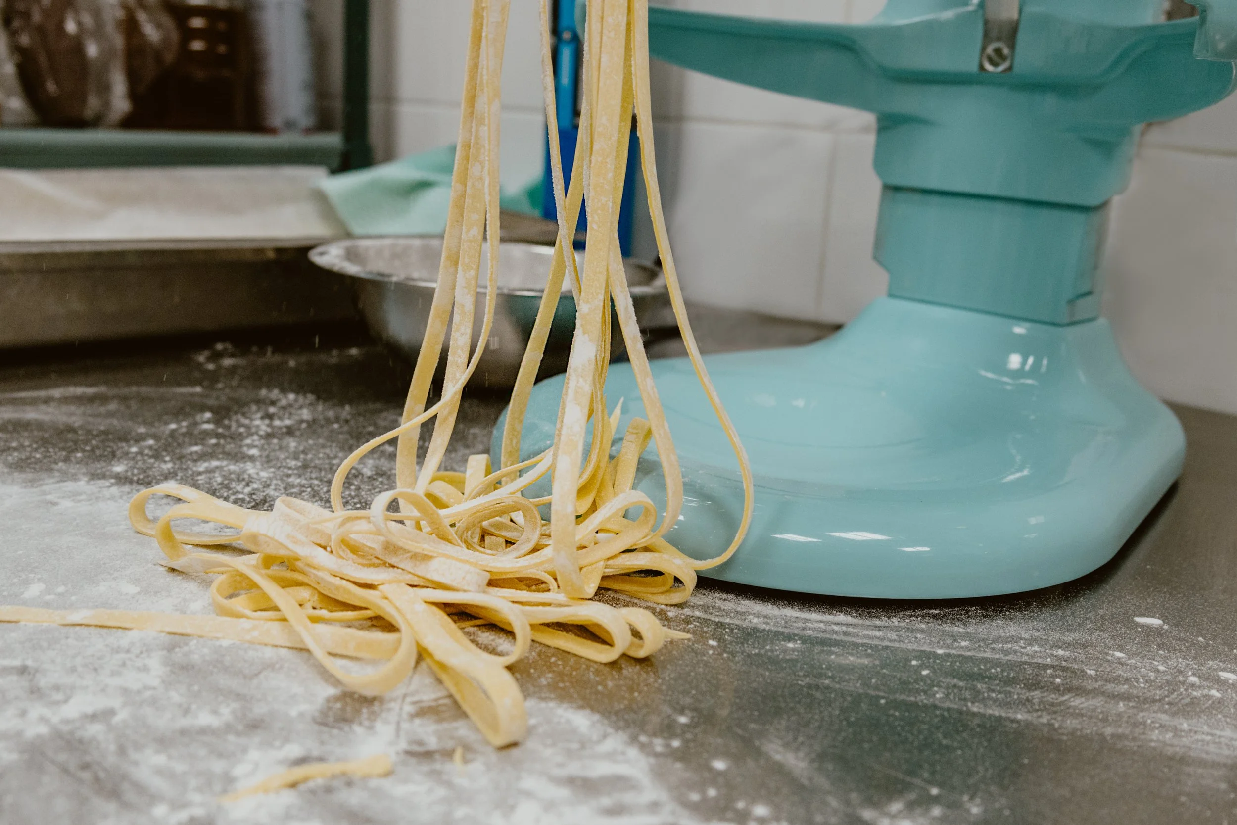 Fresh homemade pasta being prepared on Pickle Jar's kitchen counter, with a vintage teal kitchen appliance, flour scattered on the surface.