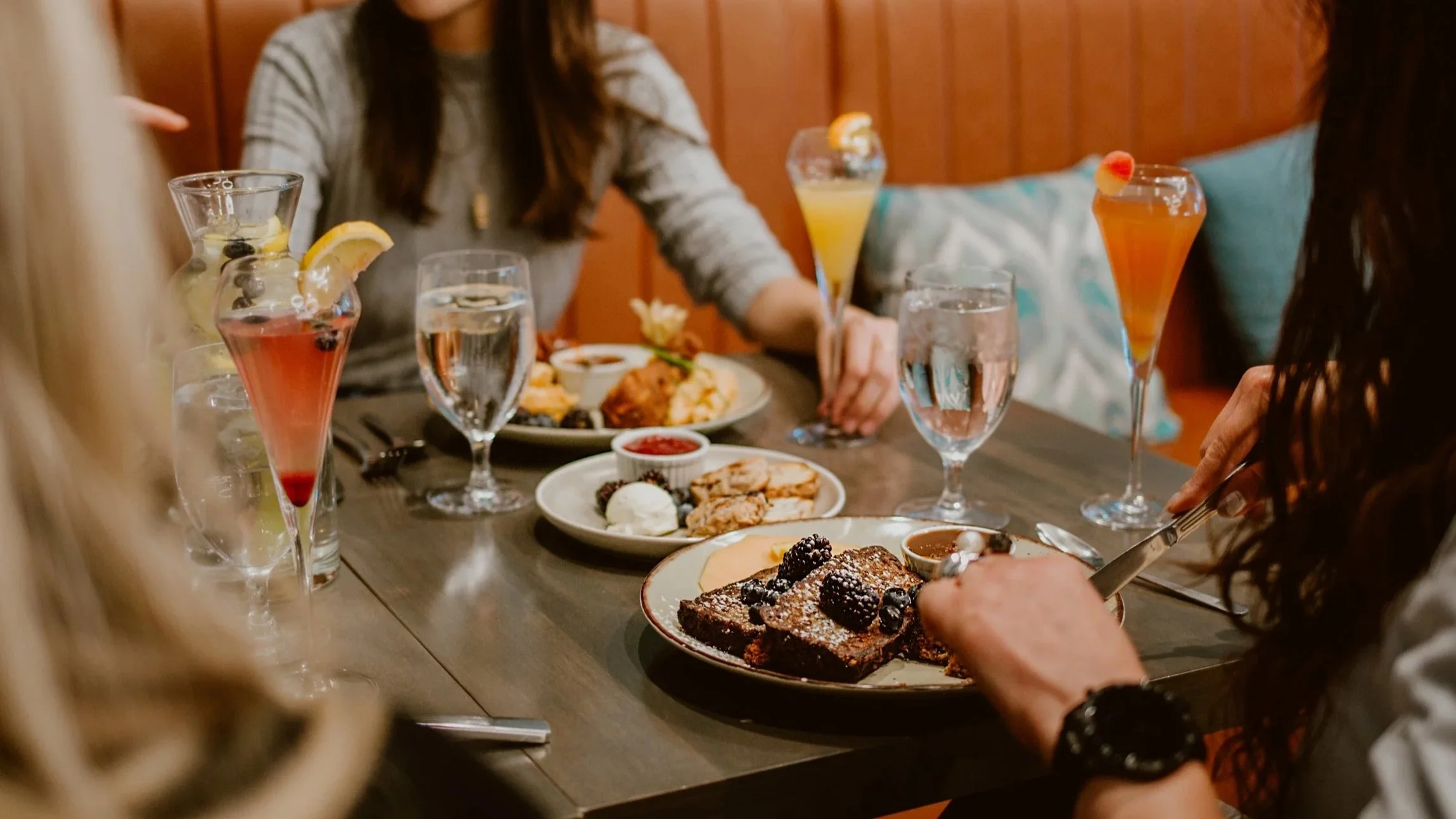 A group of women having brunch at Pickle Jar restaurant with a table full of various brunch plates and mimosa's.