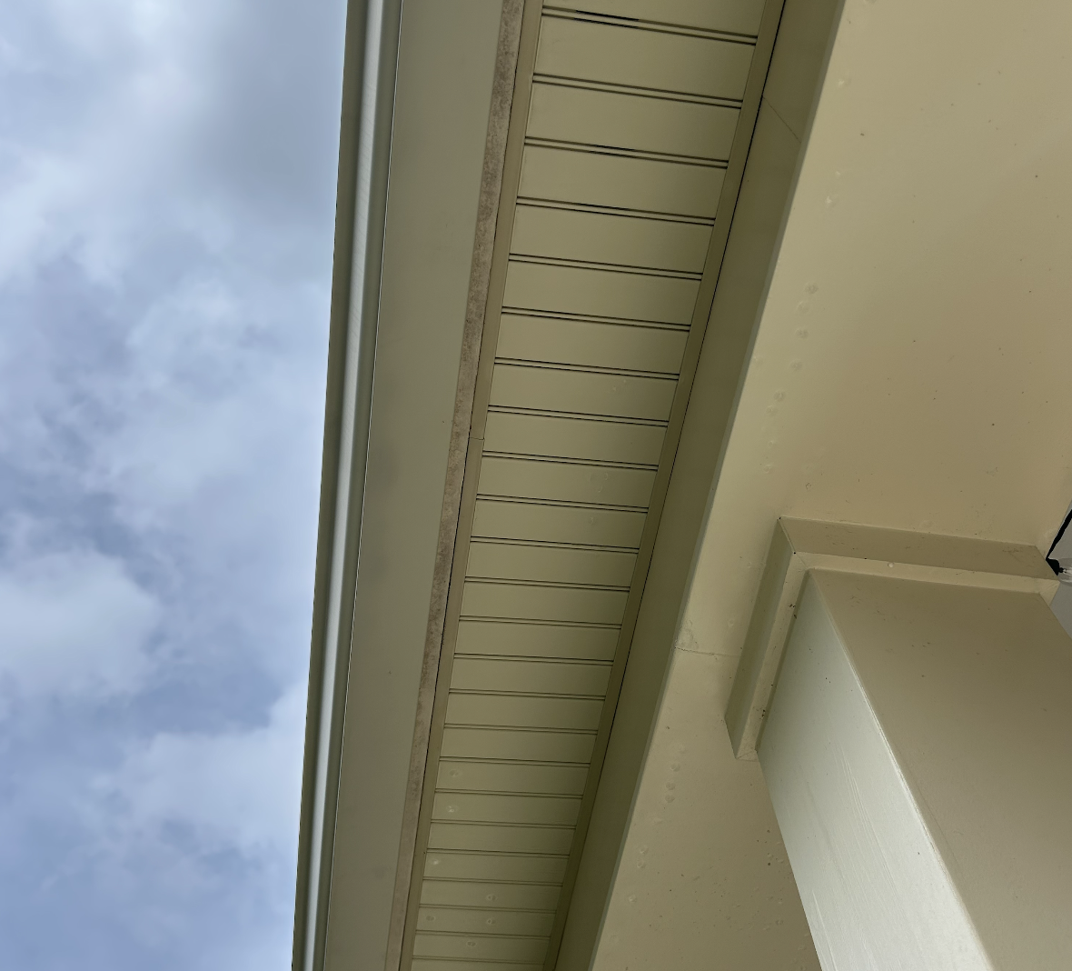Close-up of beige siding and eaves on a building with a cloudy sky in the background.