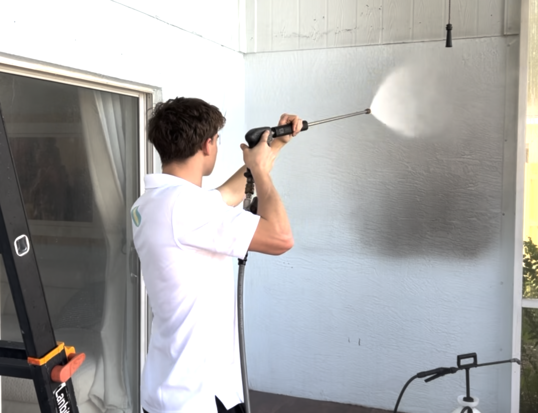 Man pressure washing a light blue exterior wall on a porch.