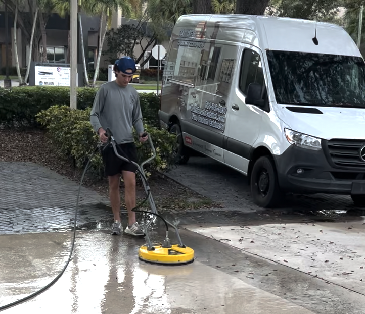 A man pressure washing a sidewalk with a yellow cleaning machine next to a white delivery van.