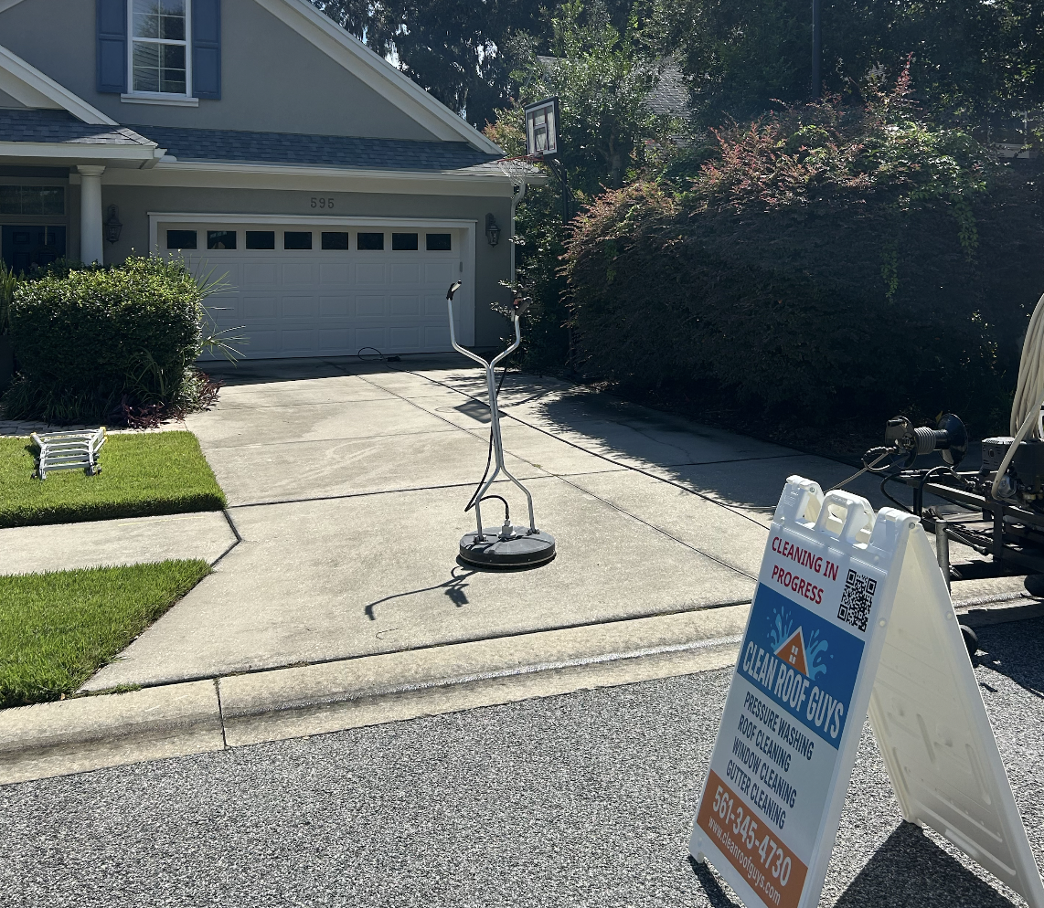 Residential driveway with cleaning equipment and a sign that reads 'Cleaning in Progress' for a roof cleaning business called 'Clean Roof Guys'.