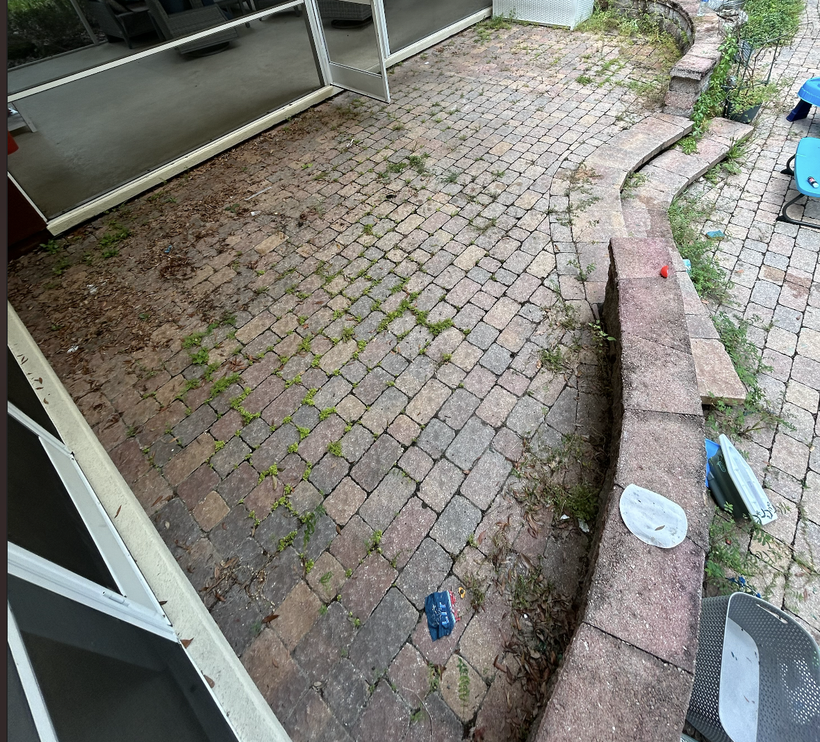 A backyard patio with cobblestone paving, a low brick wall, and scattered outdoor toys and debris.