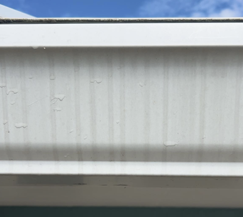 Close-up of a white window frame with water droplets on the surface, with a partial view of blue sky and clouds in the background.
