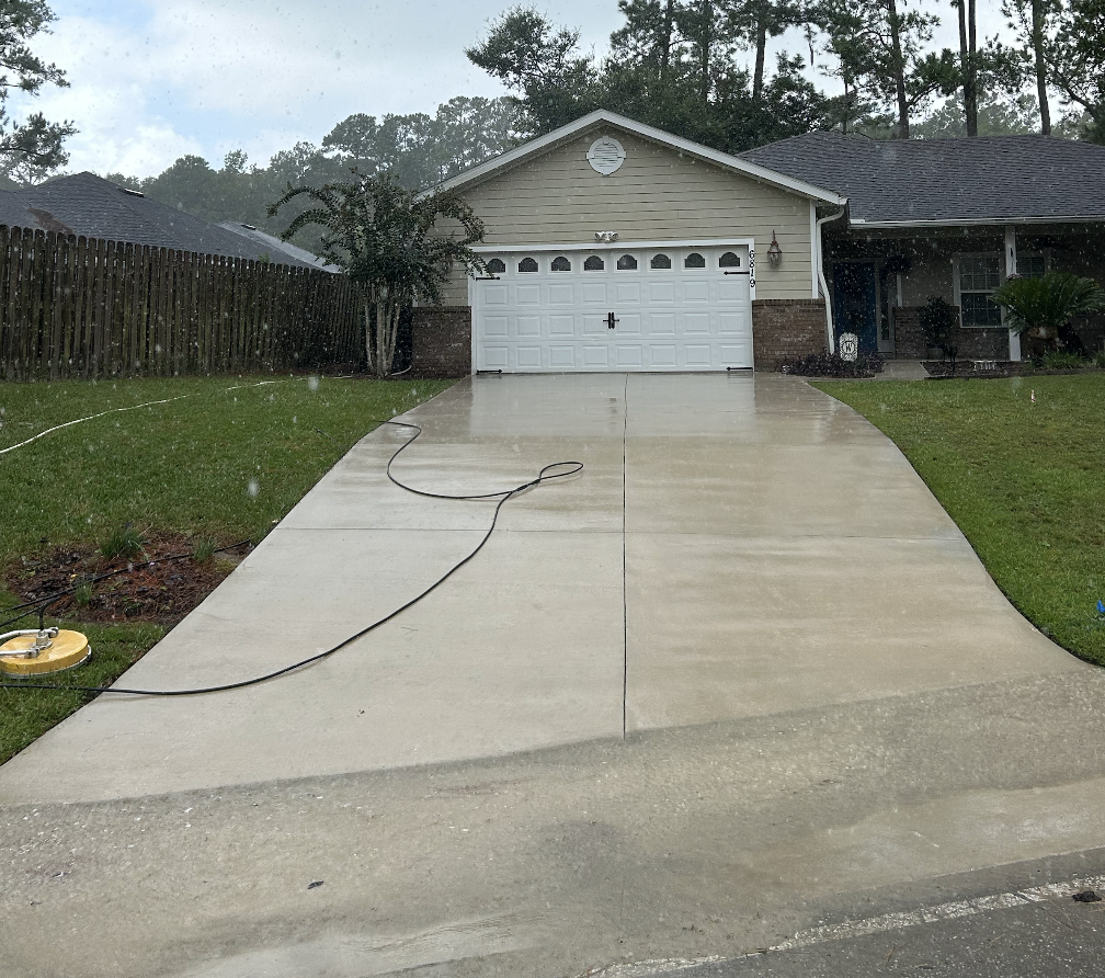 Rainy day view of a suburban house with a driveway and a closed garage door, wet from rain, with a hose on the driveway.
