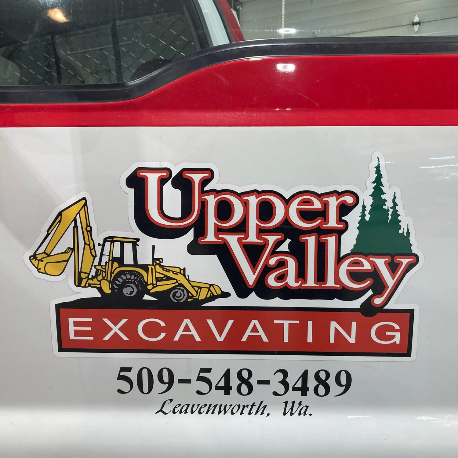 Sticker for Upper Valley Excavating in Leavenworth, Washington, featuring a yellow excavator and green trees.
