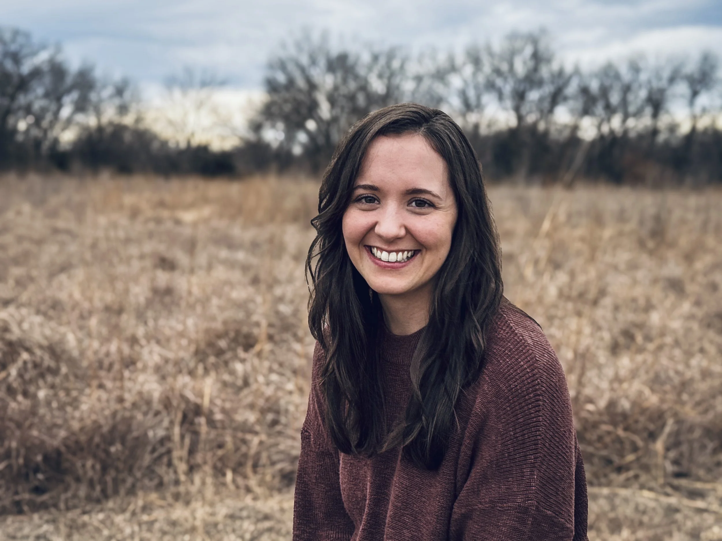 Professional headshot of Jenna Yutzy, licensed acupuncturist at Taproot Acupuncture & Herbal Medicine, smiling outdoors in a natural Kansas landscape setting.