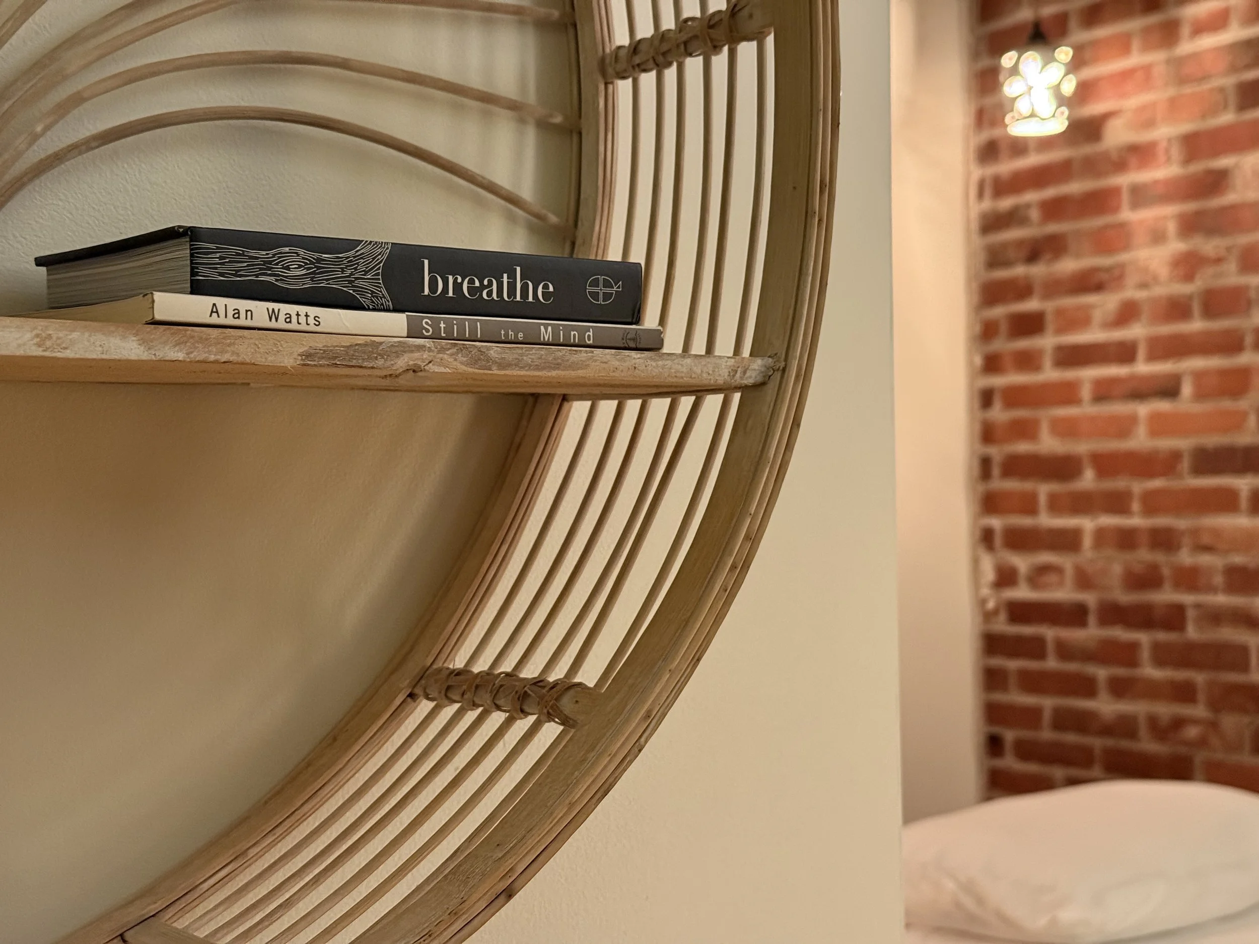 A peaceful view into the treatment room at Taproot Acupuncture & Herbal Medicine in Newton, KS. A wooden shelf displays books titled 'Still the Mind' and 'Breathe' against a backdrop of historic red brick and soft lighting.