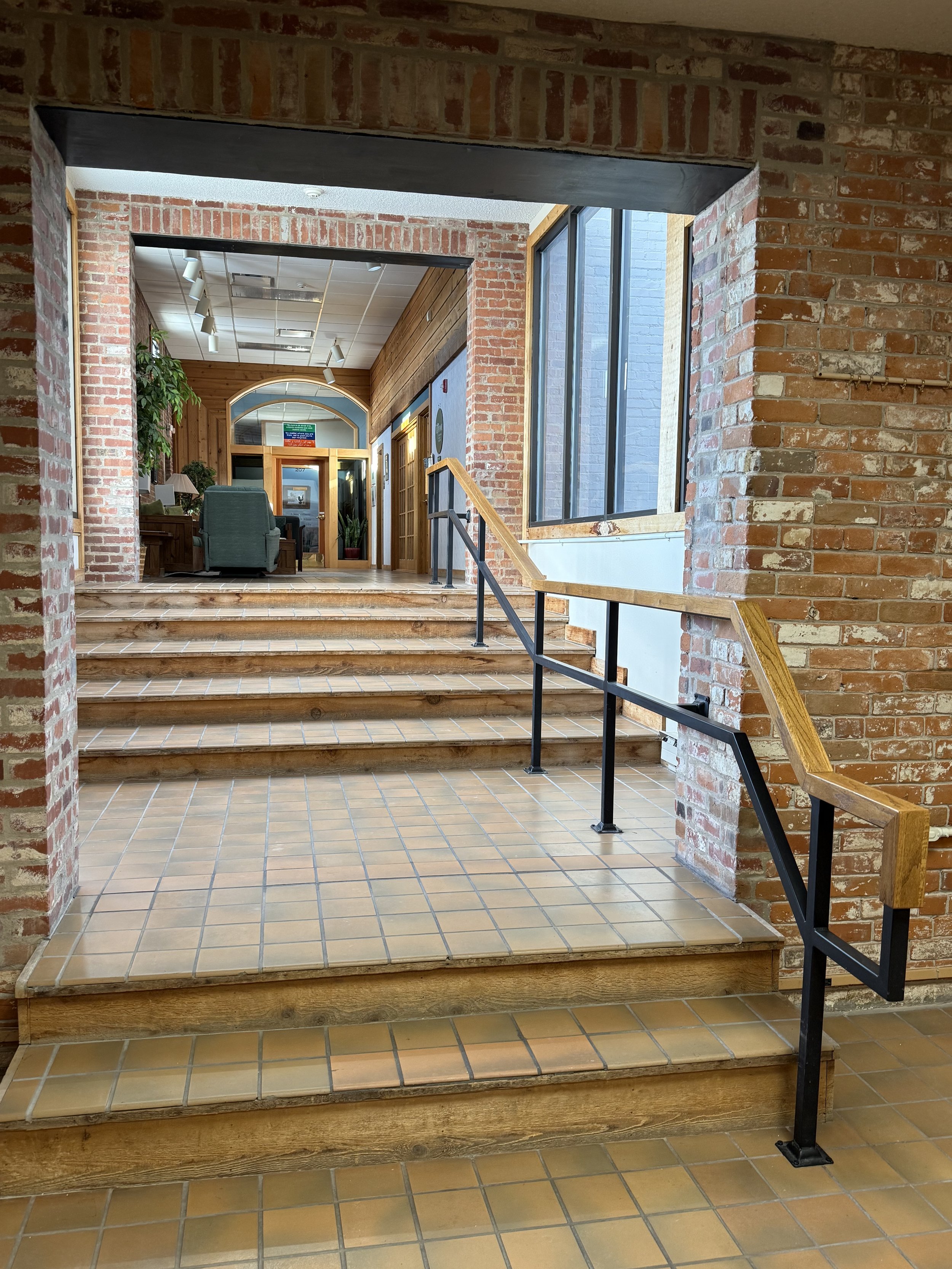 A bright, sun-filled historic brick staircase on the second floor of the Old Mill Plaza leading to Taproot Acupuncture & Herbal Medicine. Please note that while the building has an elevator, this specific clinic entrance is not wheelchair accessible.