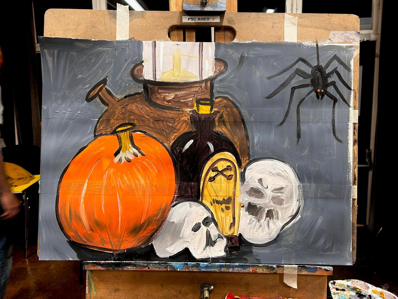 Painting of a Halloween still life featuring a pumpkin, skulls, a potion bottle, a candle, and a spider.
