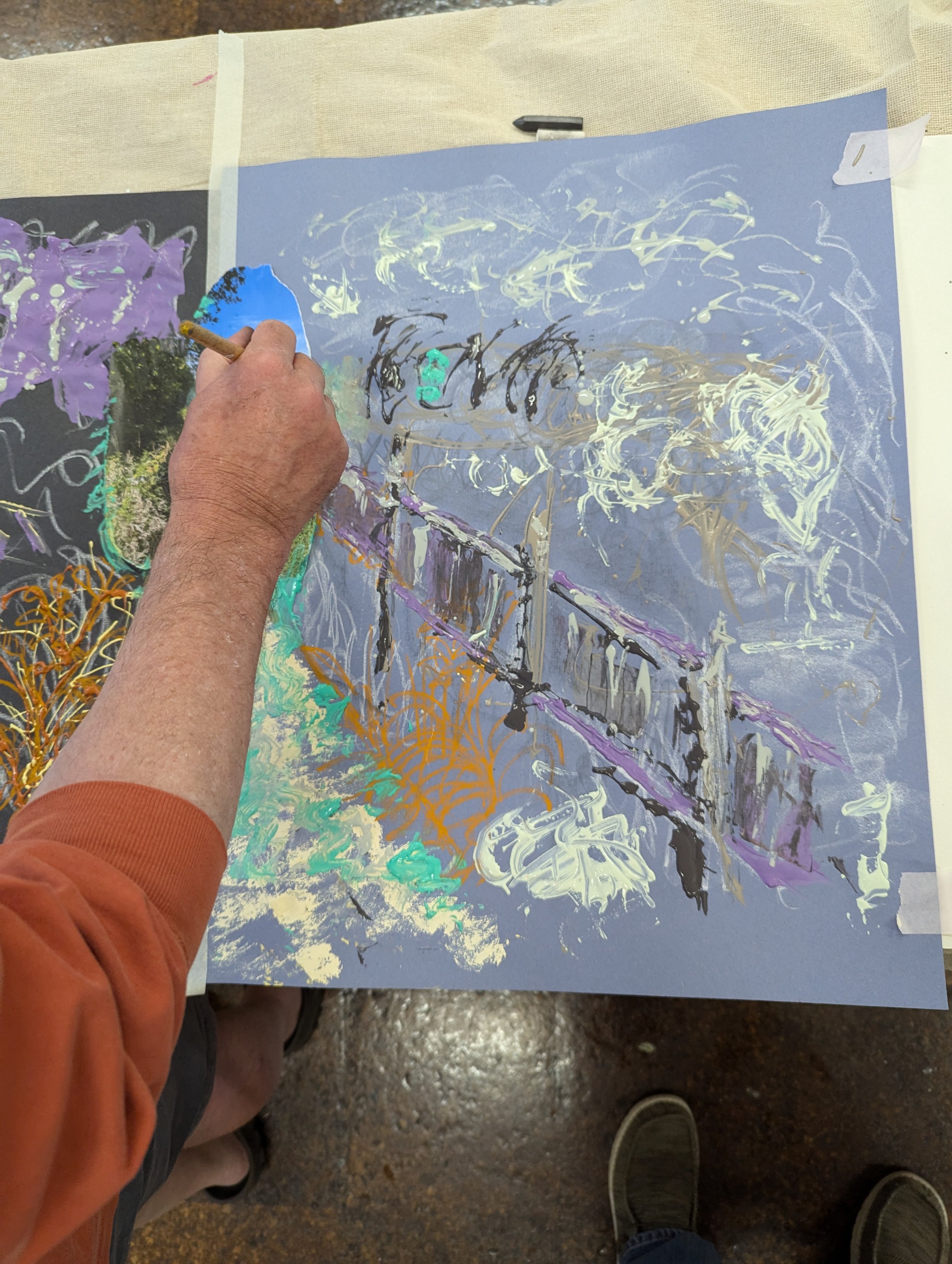 A student painting an abstract landscape on a blue sheet of paper 