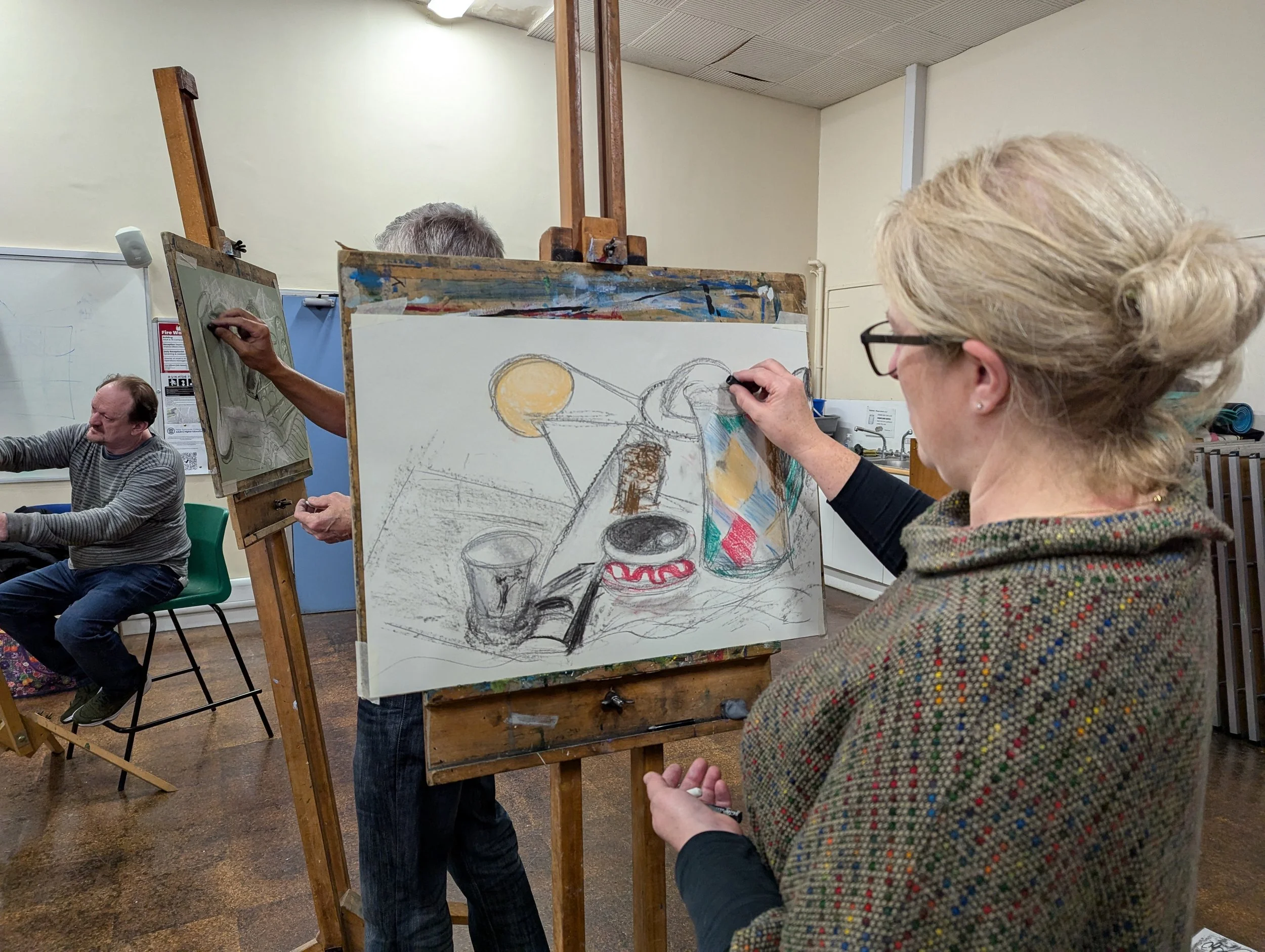 Student painting a still life scene on canvas at an art class. 