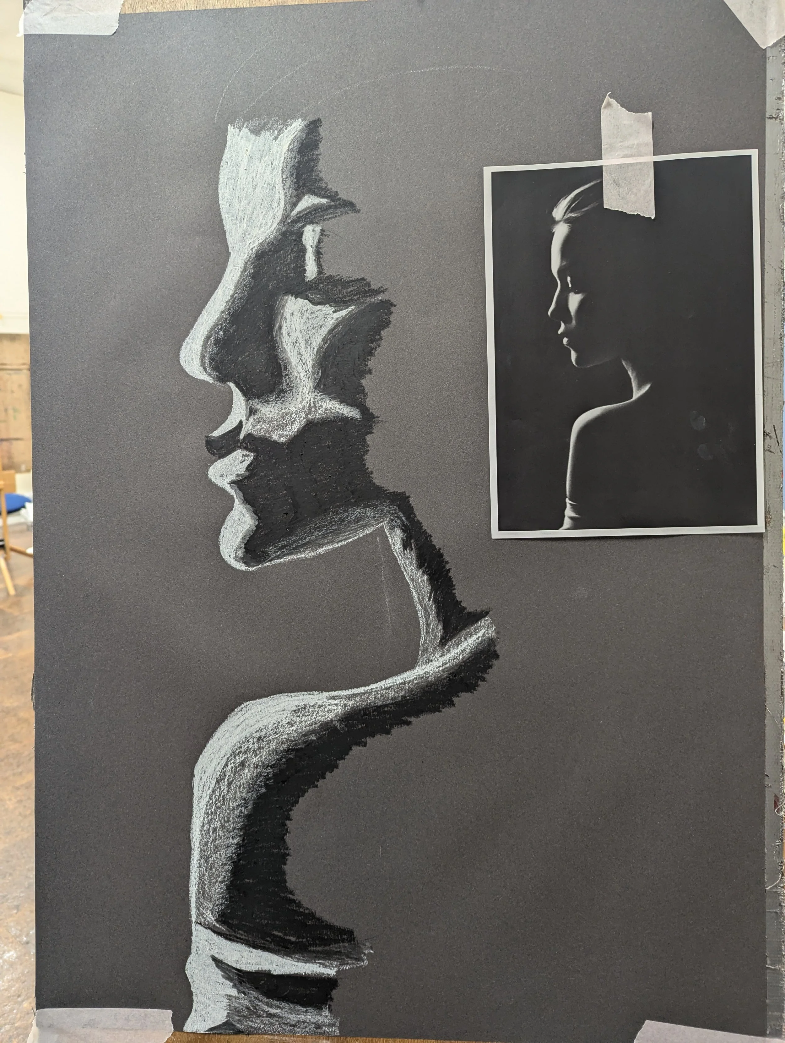 A black and white chalk drawing of a woman's face in profile on a gray background, with a printed photo of an illuminated woman's face pinned to the upper right side of the drawing.