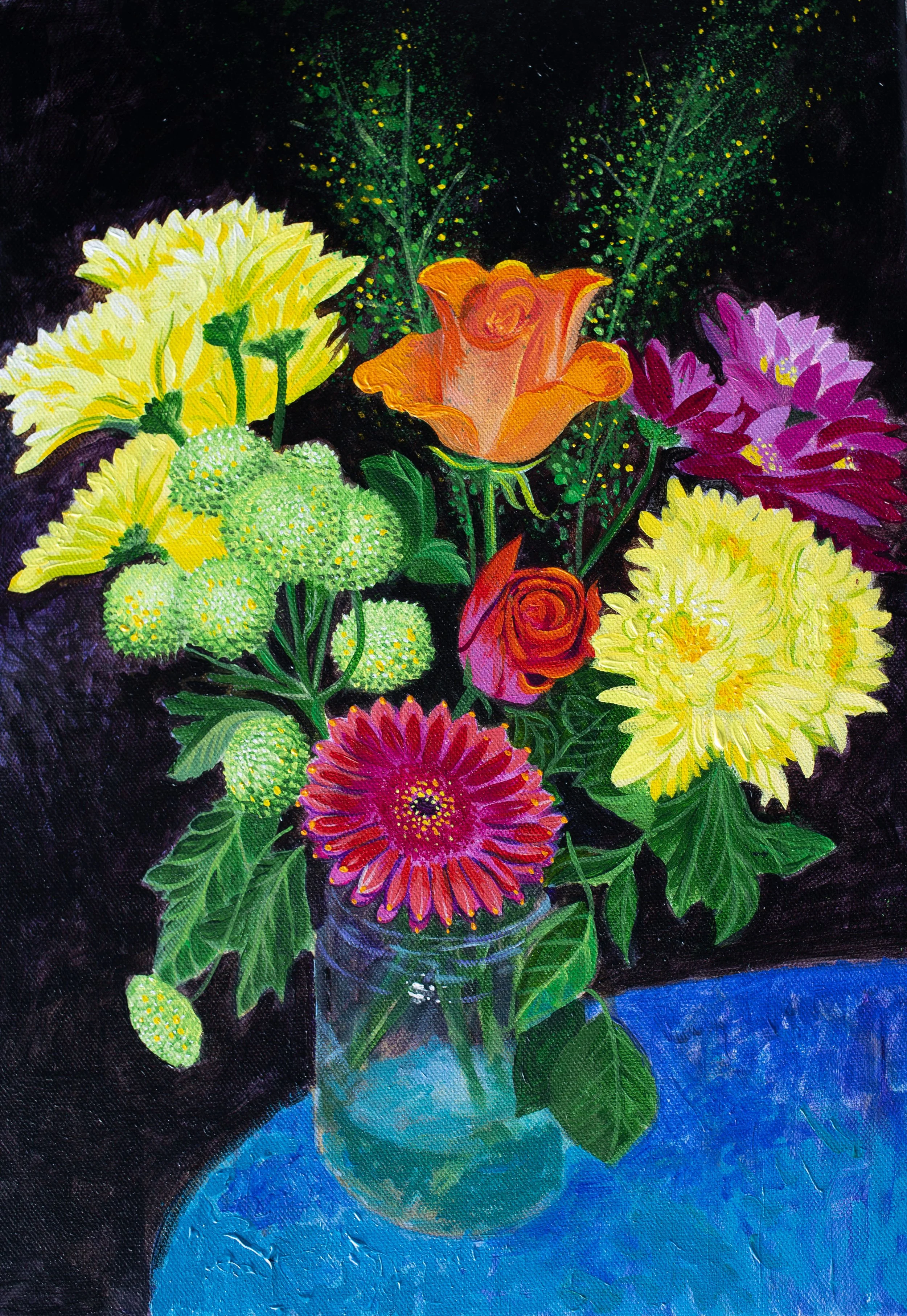 A vibrant bouquet of various colourful flowers set in a clear glass vase on a blue table, set against a dark background.