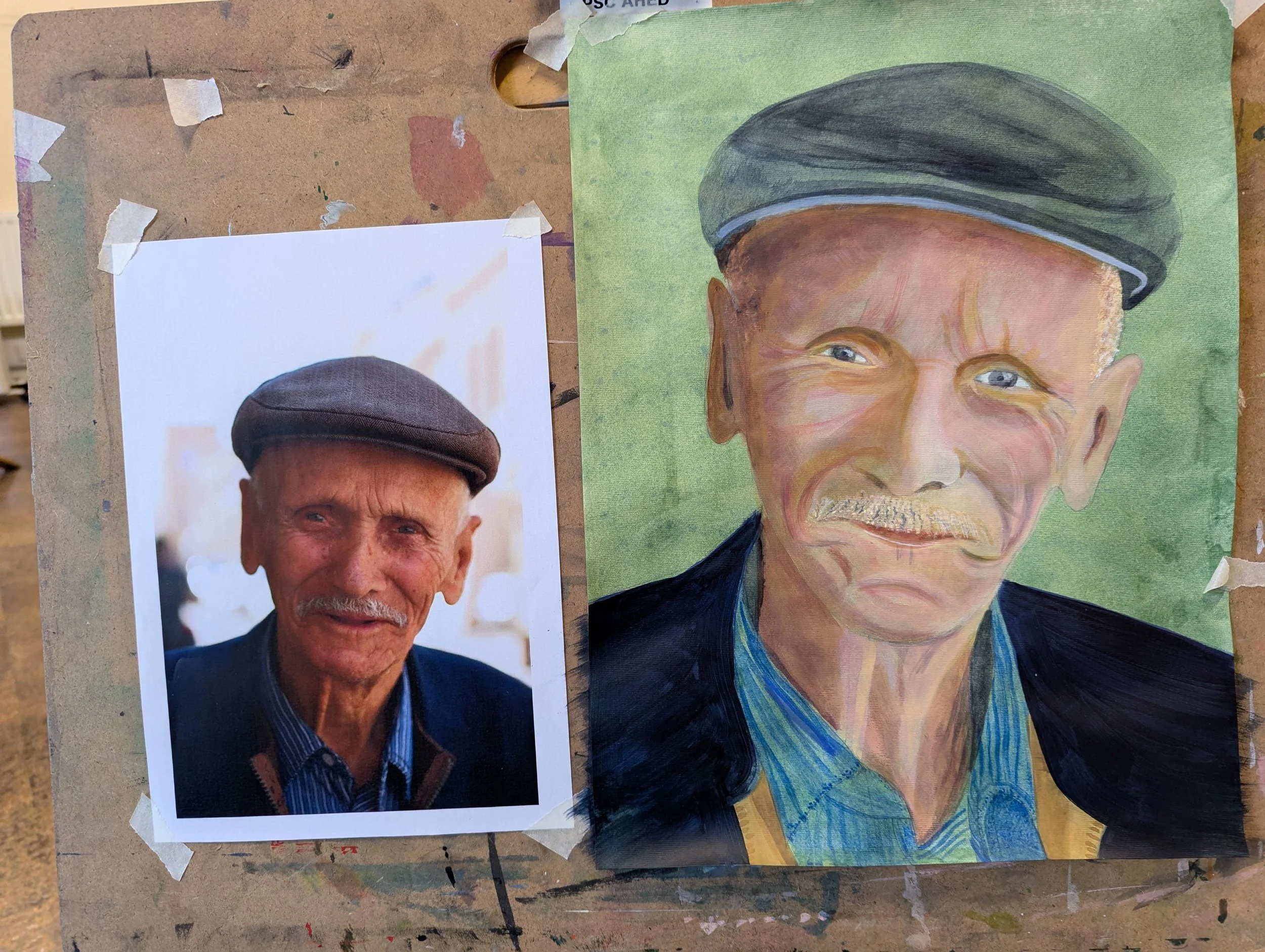 A colored portrait painting of an elderly man wearing a cap, with a mustache, blue eyes, and a slight smile, situated on a green background, next to a printed photograph of the same man.