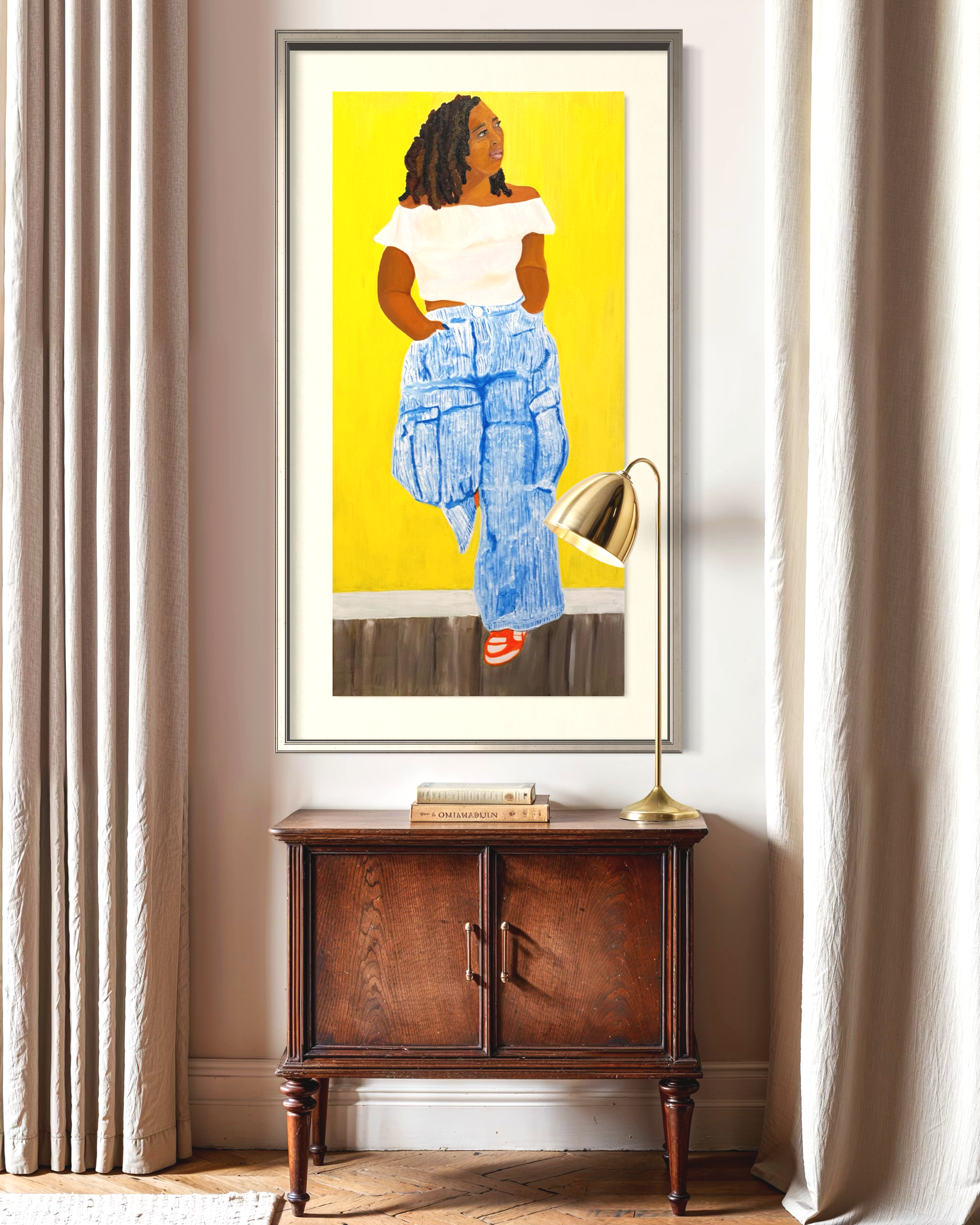 A framed painting of a woman with curly hair, wearing a white off-the-shoulder top and blue patterned pants, standing with her hands in her pockets against a yellow background. The painting is displayed on a wall between two beige curtains, with a wooden cabinet below it and a gold-colored lamp resting on the cabinet, illuminating the painting.