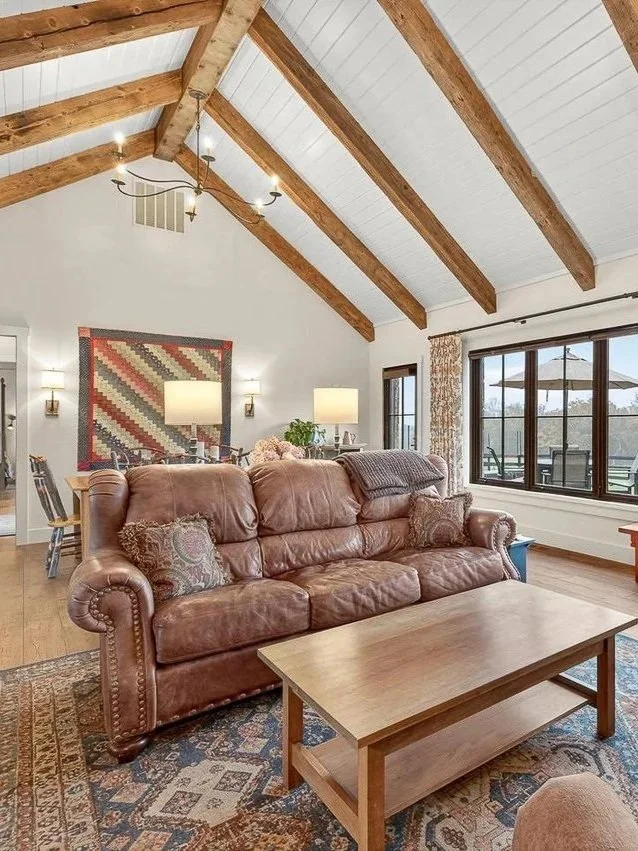 Living room with a leather sofa, wooden coffee table, large window, and exposed wooden beams on the ceiling.