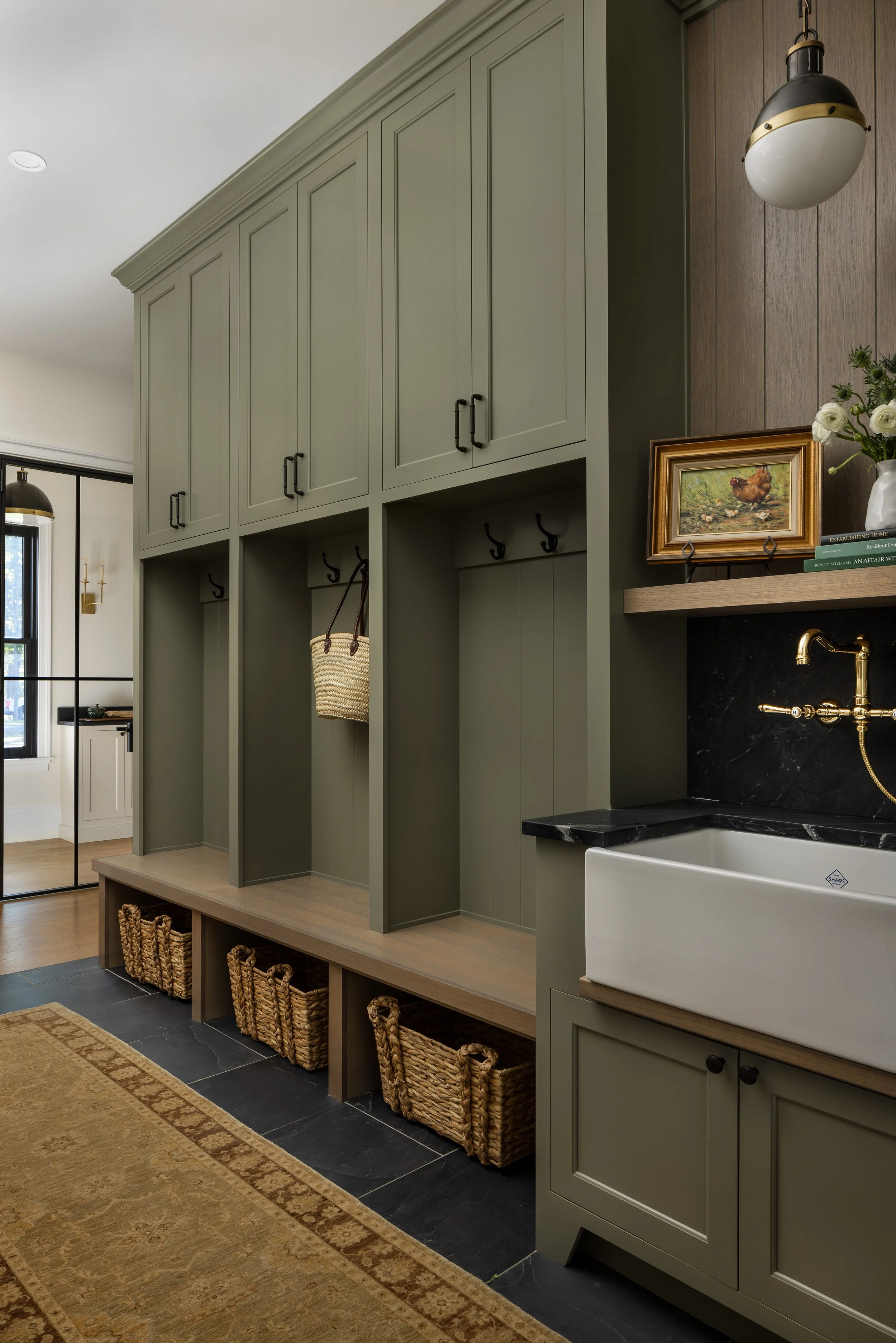 Entryway with built-in storage and hooks, wicker baskets, a farmhouse sink, black countertop, and decorative items on a shelf.