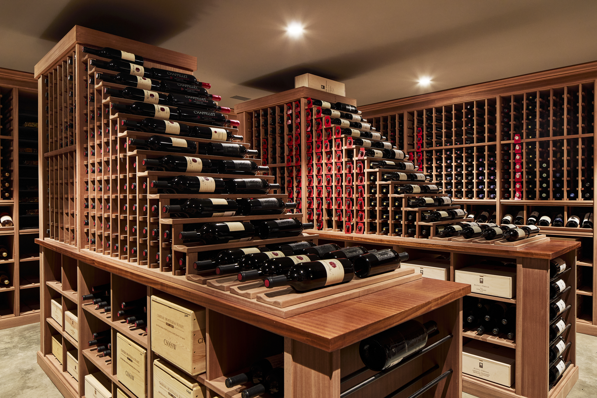 A wine cellar with wooden racks filled with bottles of wine, illuminated by ceiling lights.