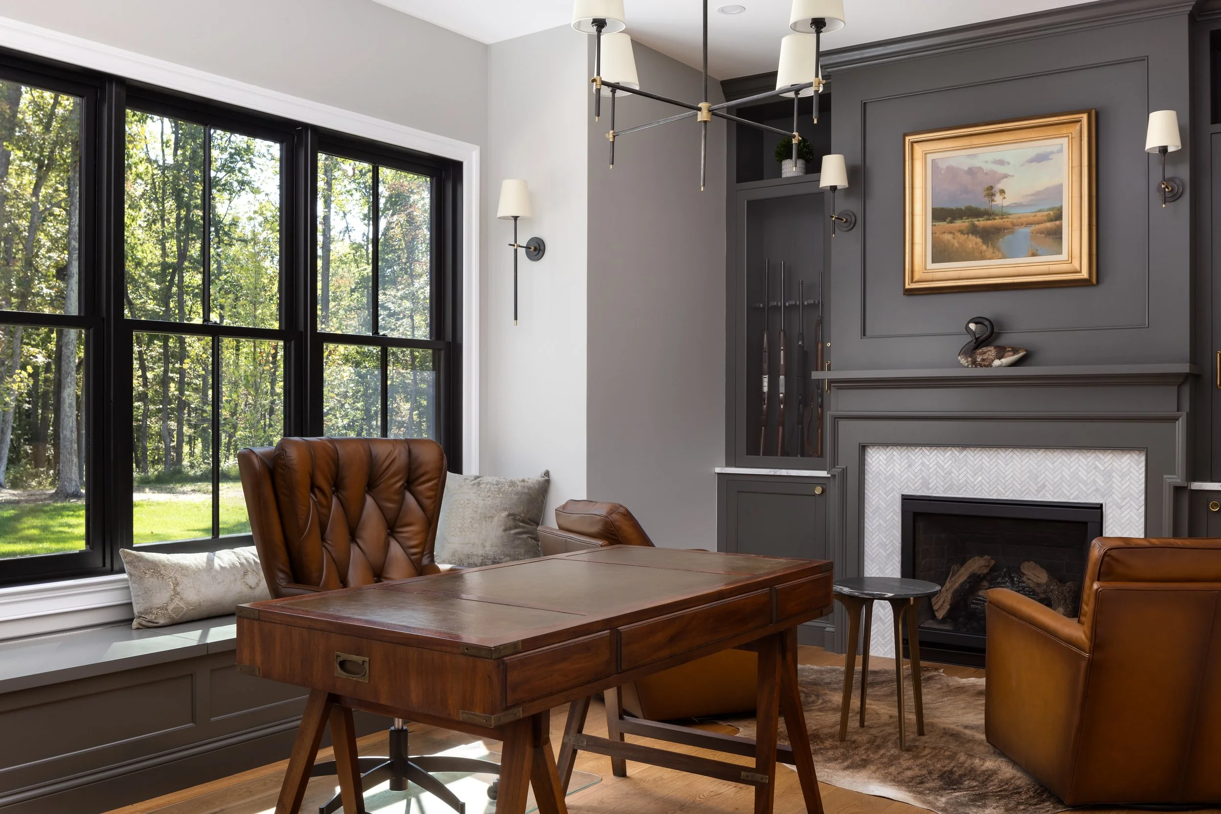 Living room with large window, brown leather chair, fireplace, dark gray built-in cabinetry, landscape painting, and decorative duck sculpture.