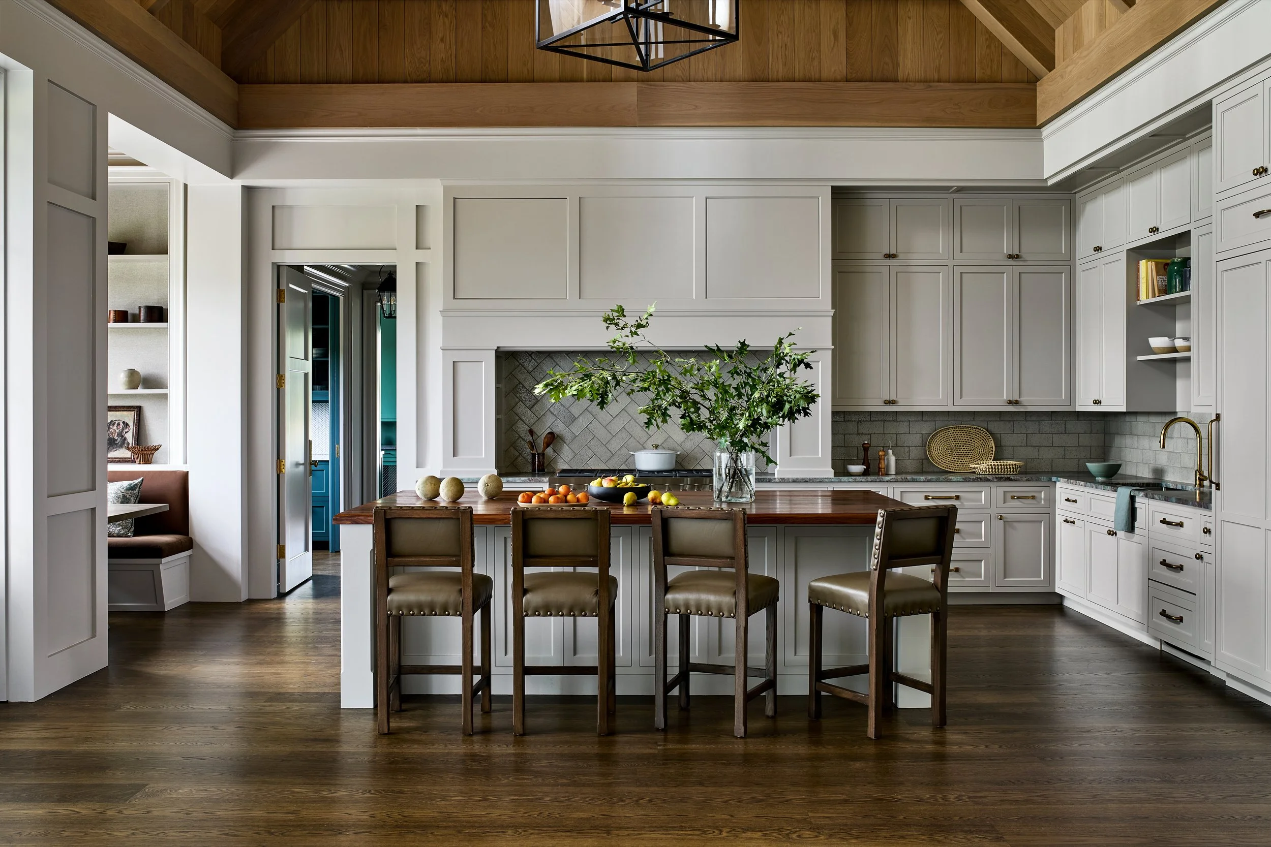 Modern kitchen with white cabinetry, wooden countertop island, a vase with green foliage, and bar stools, with a hardwood floor and a wooden ceiling.