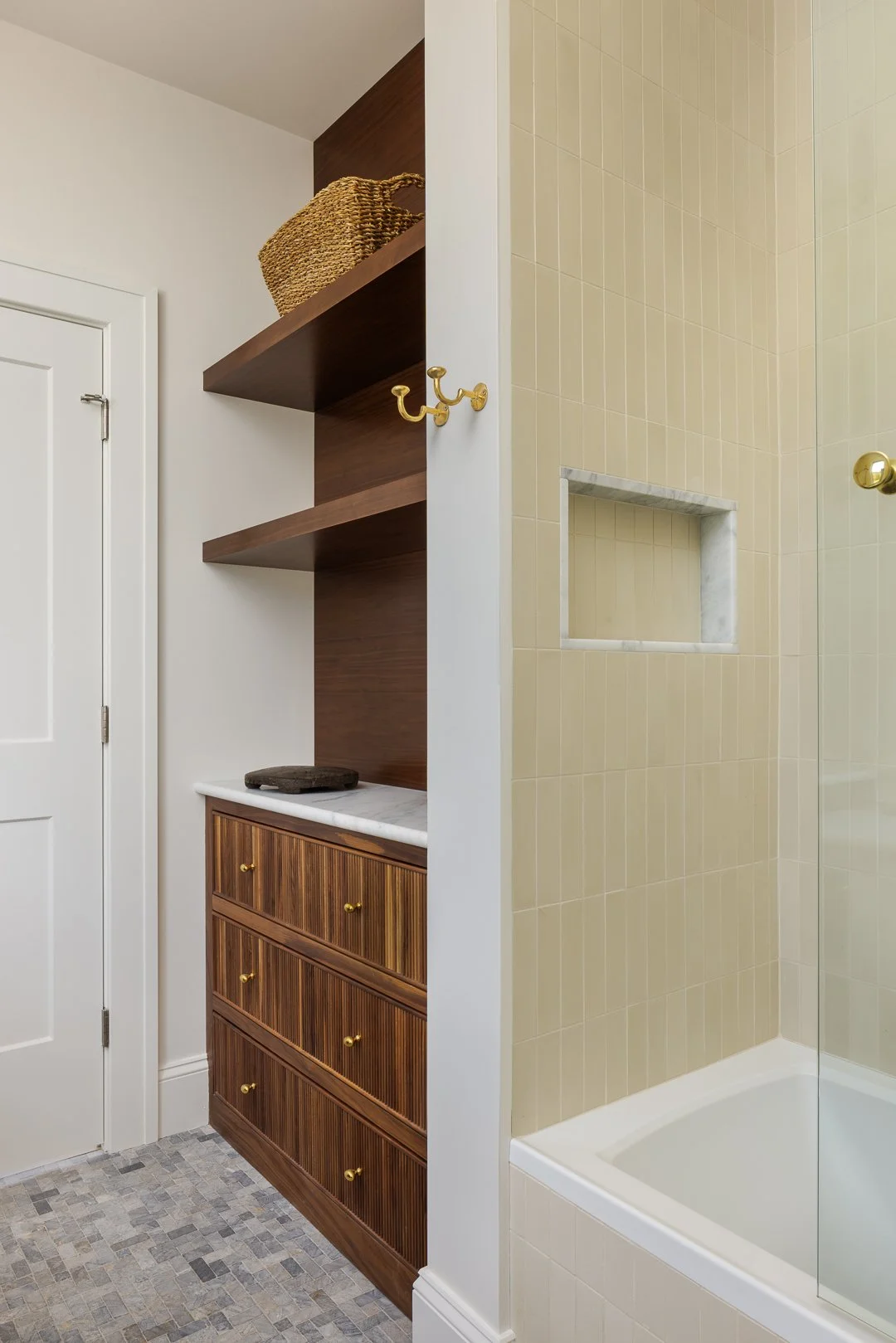 Bathroom with a wooden cabinet and open shelves, a marble countertop, and a glass-enclosed shower with beige tiled walls.