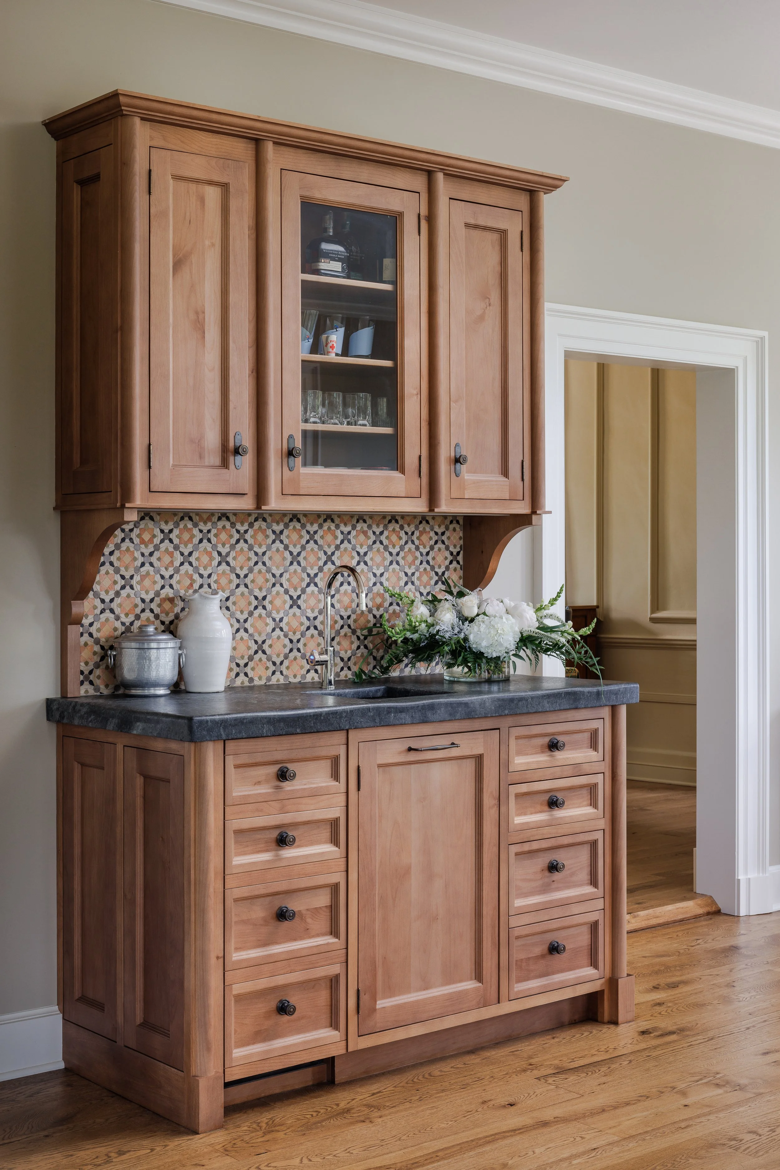 Wooden kitchen cabinet with patterned backsplash, a sink, and a floral arrangement.