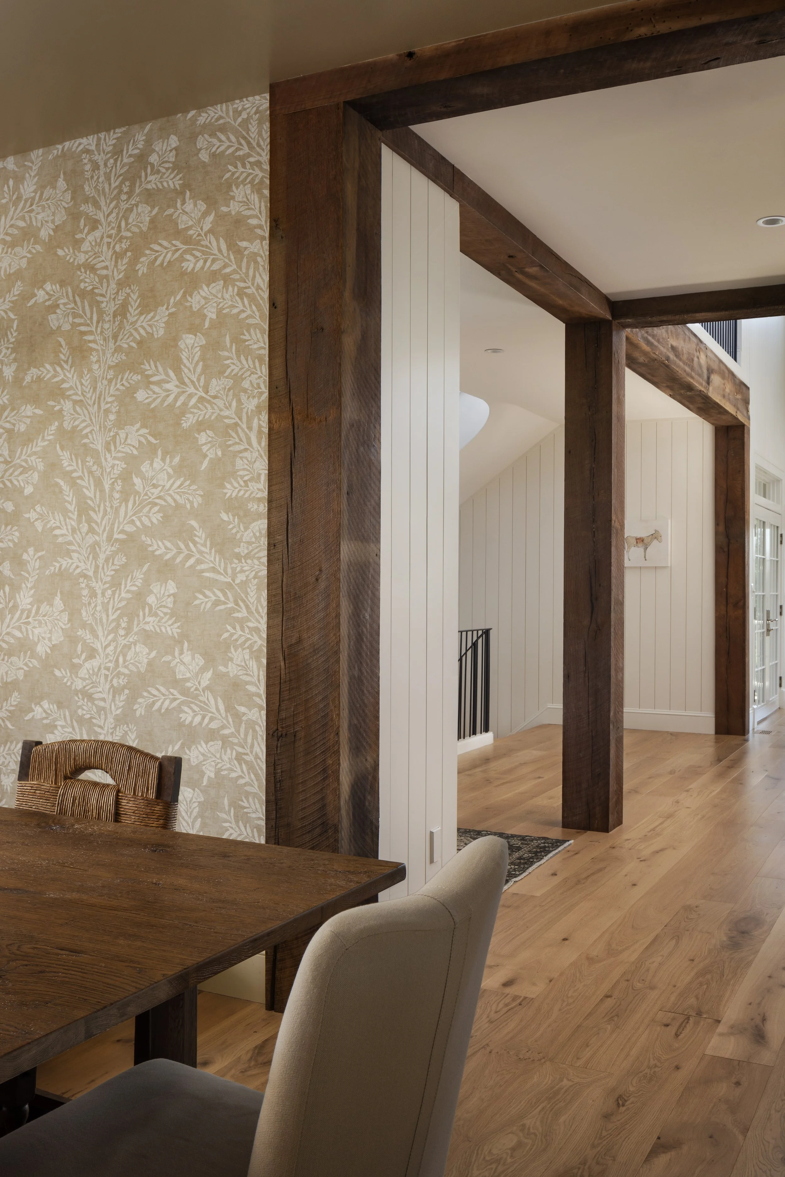 Interior view of a home with wooden and white wall paneling, hardwood flooring, and part of a dining table with chairs.