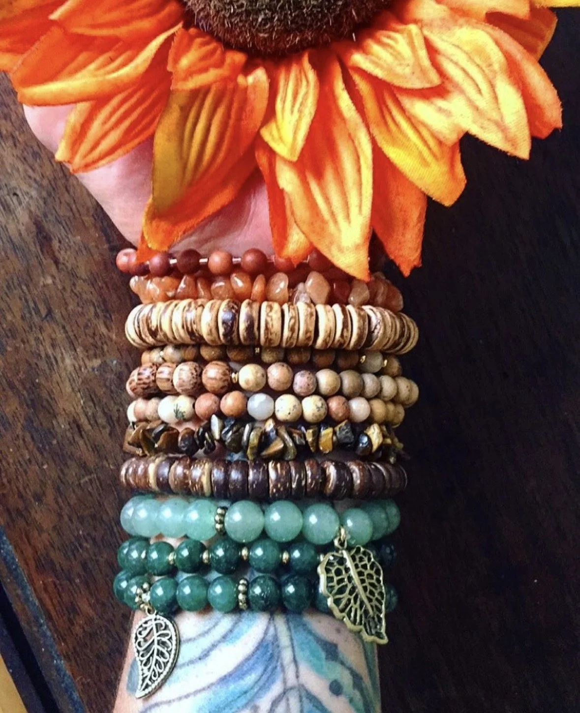 Elemental inspired beaded wood and crystal bracelets on a tattooed arm holding a sunflower